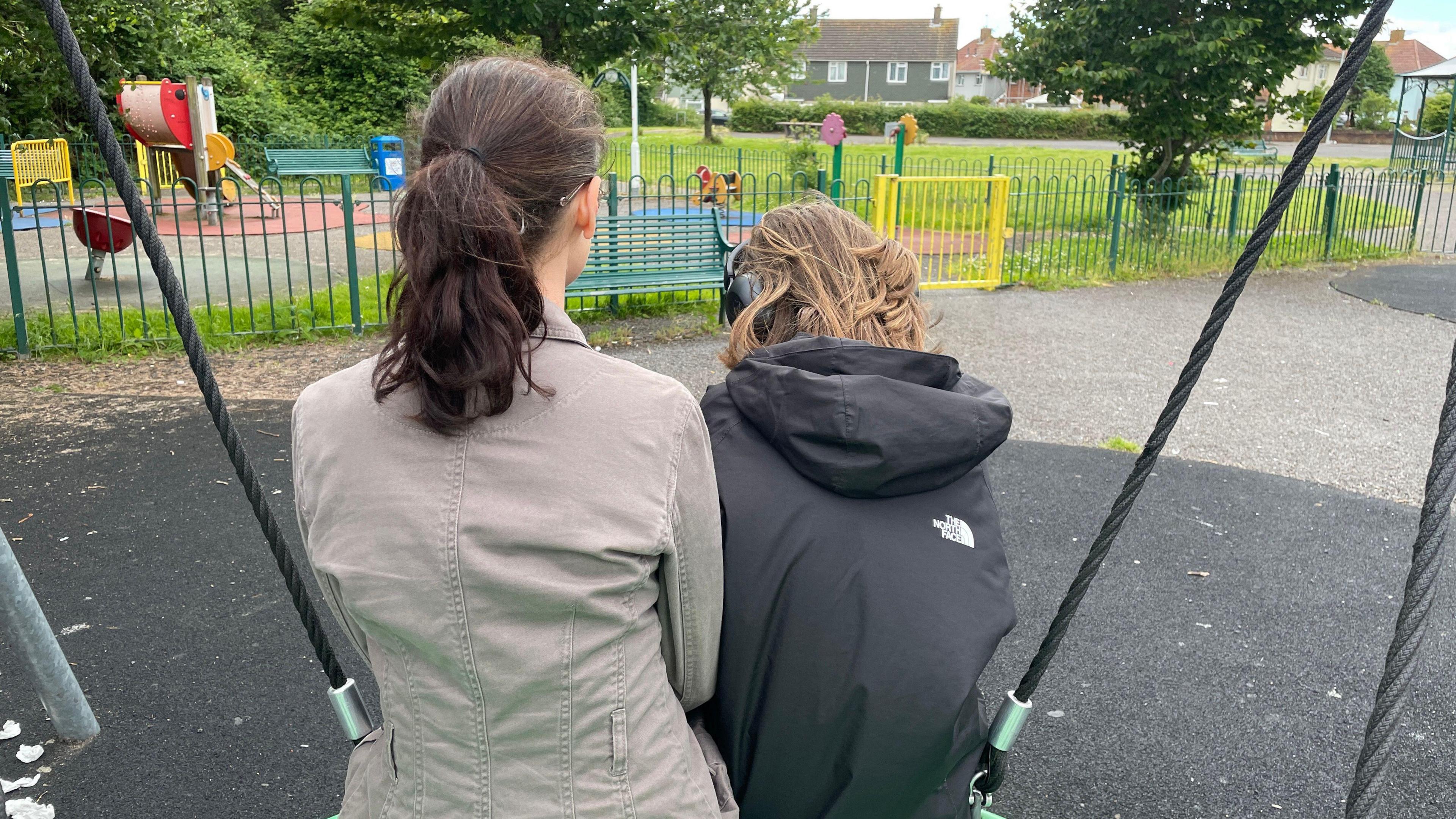 Mum and daughter sitting on swing with back to camera