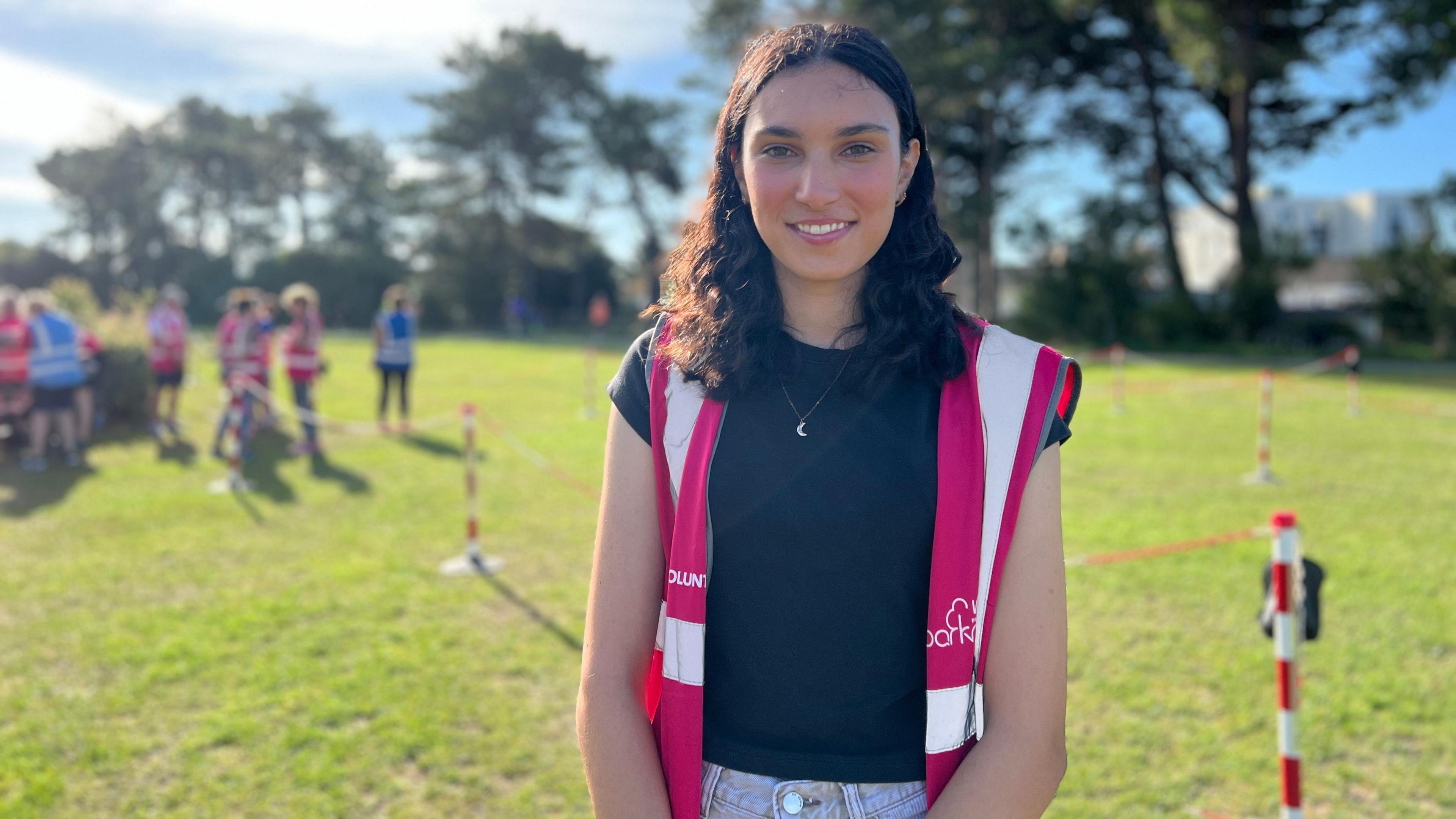 Saesha smiles at the camera wearing a highviz Parkrun vest as volunteers get ready behind her