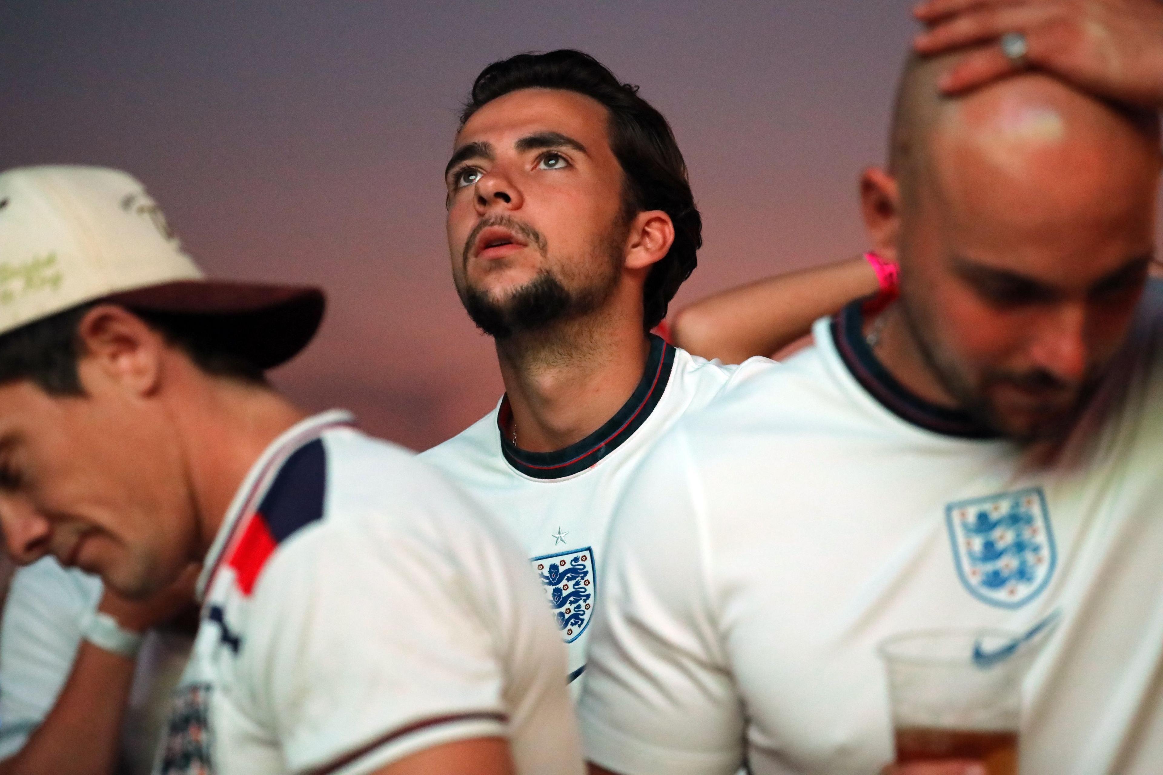 Three men in England shirts look sad. One is looking upwards towards the screen, another is holding his head in his hands and the third is clutching the back of his neck looking downwards.