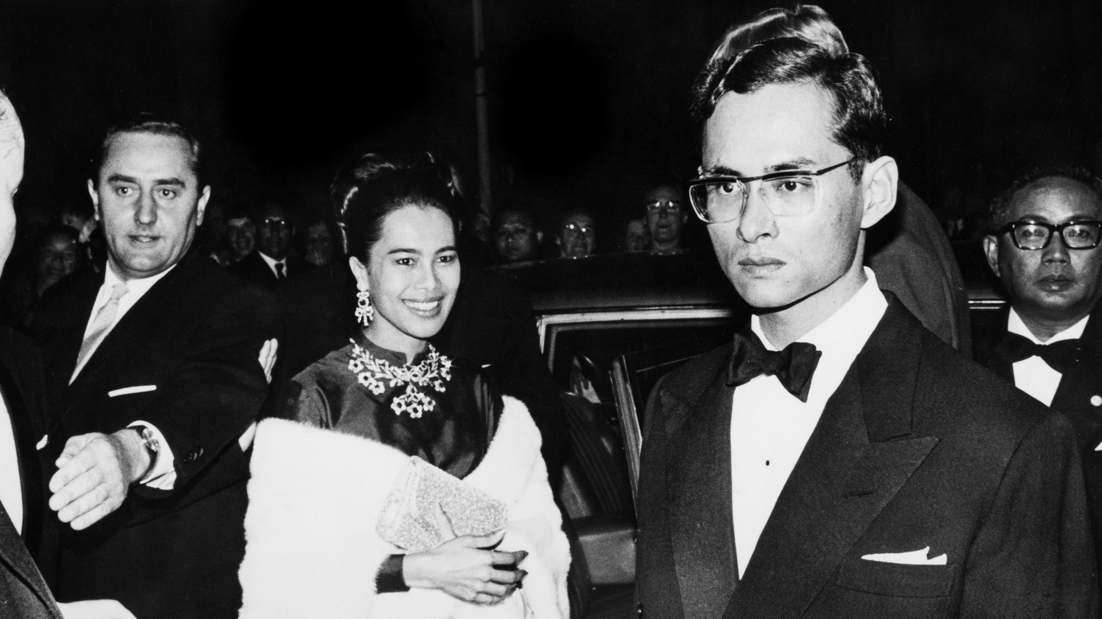 Sirikit, in a white shawl, smiles to the camera in a black and white photograph.
