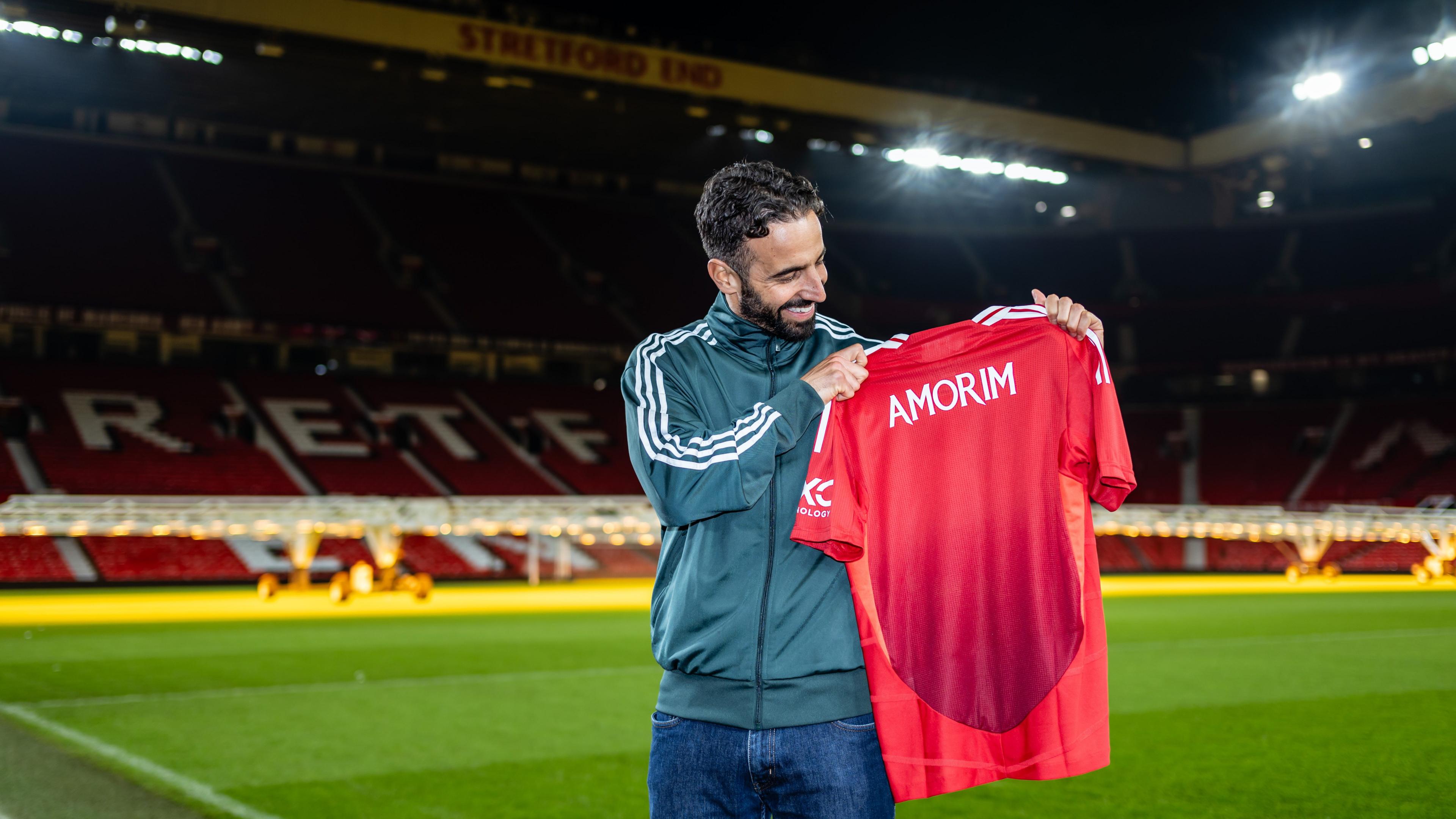 Ruben Amorim holding a Manchester United shirt up in front of the Stretford End at Old Trafford