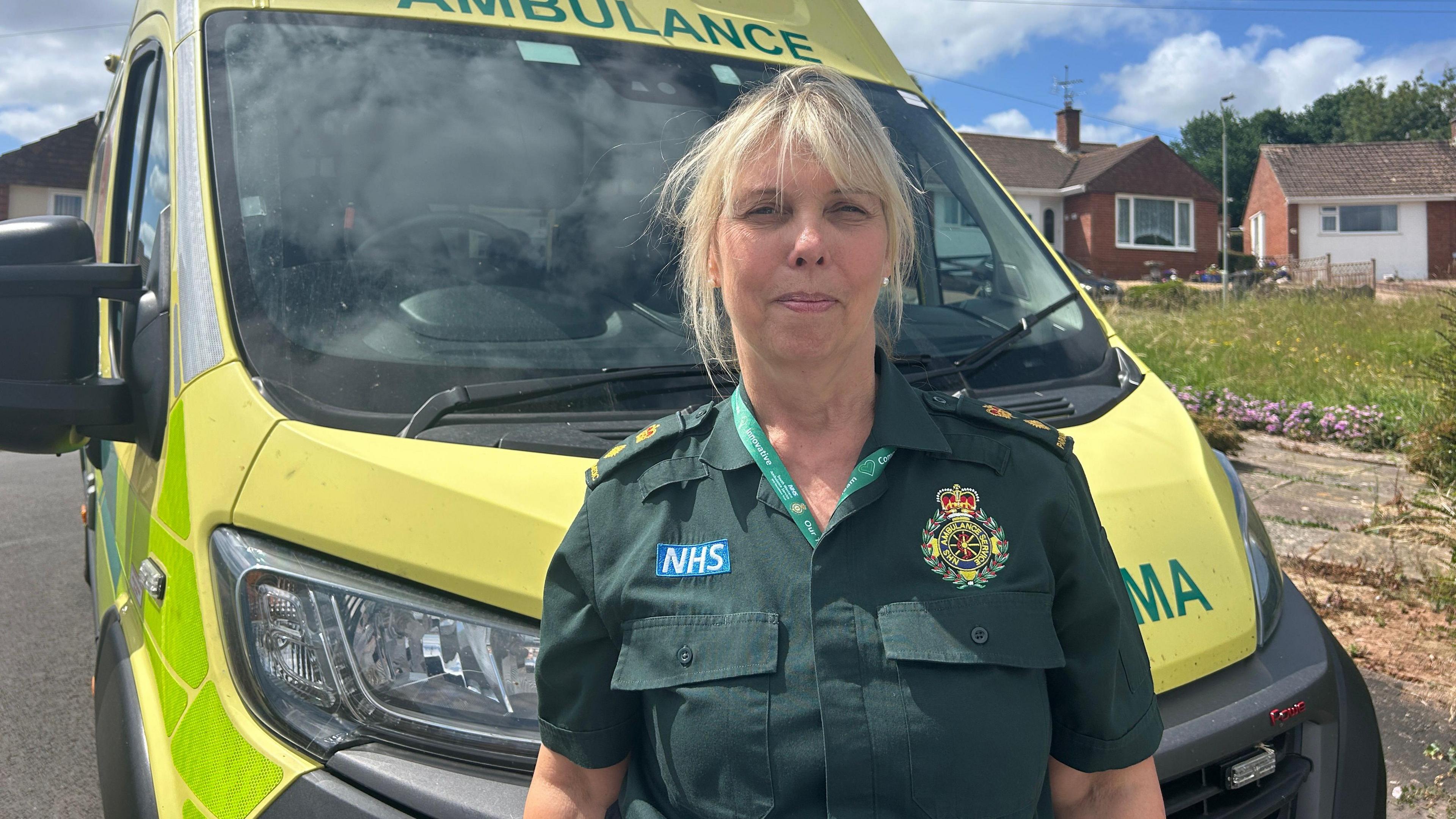 A woman in a green ambulance shirt standing in front of an ambulance