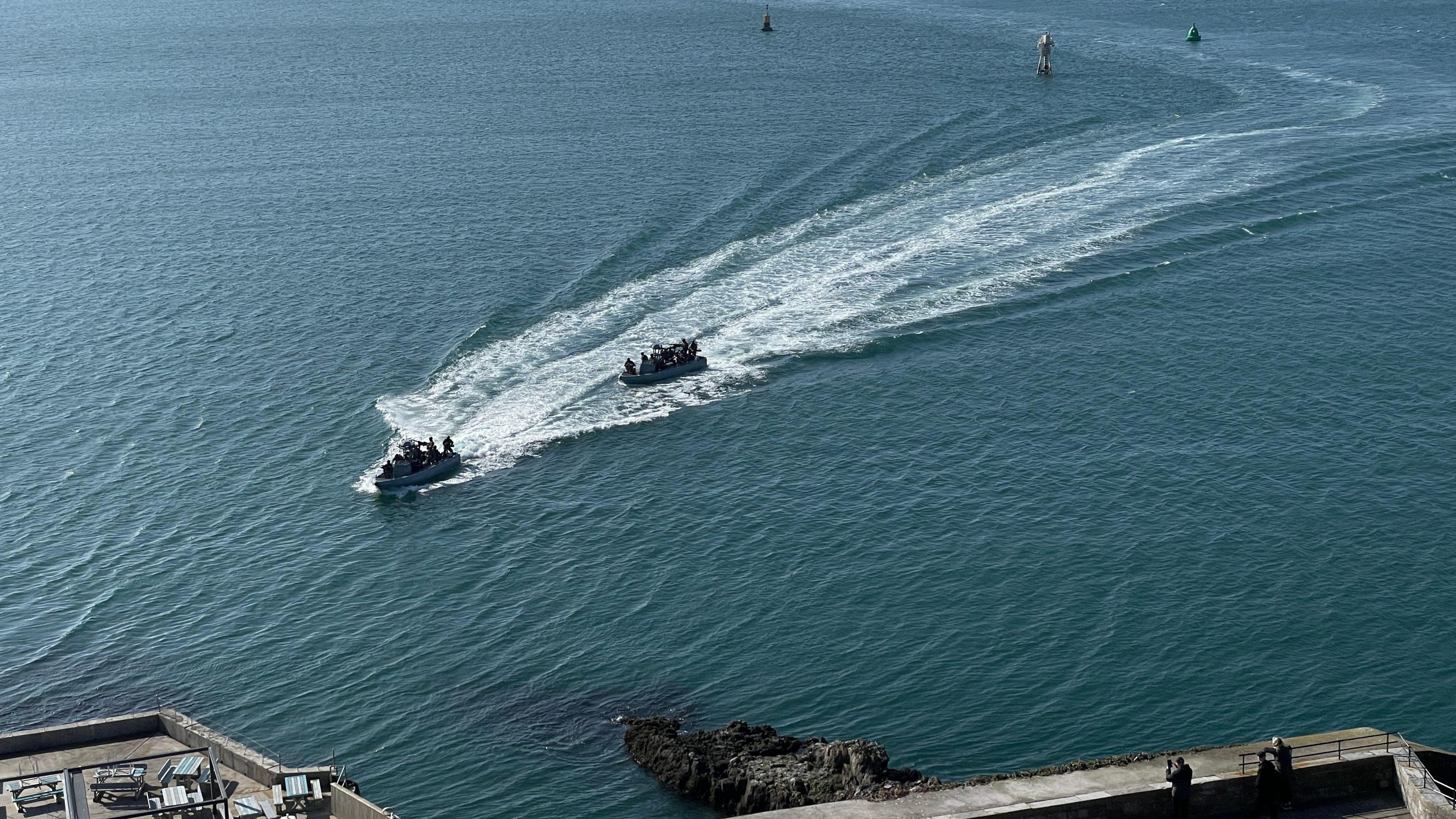 Royal Marines on board two high-speed boats come across the water in Plymouth Sound on a sunny day. Three buoys are behind them.