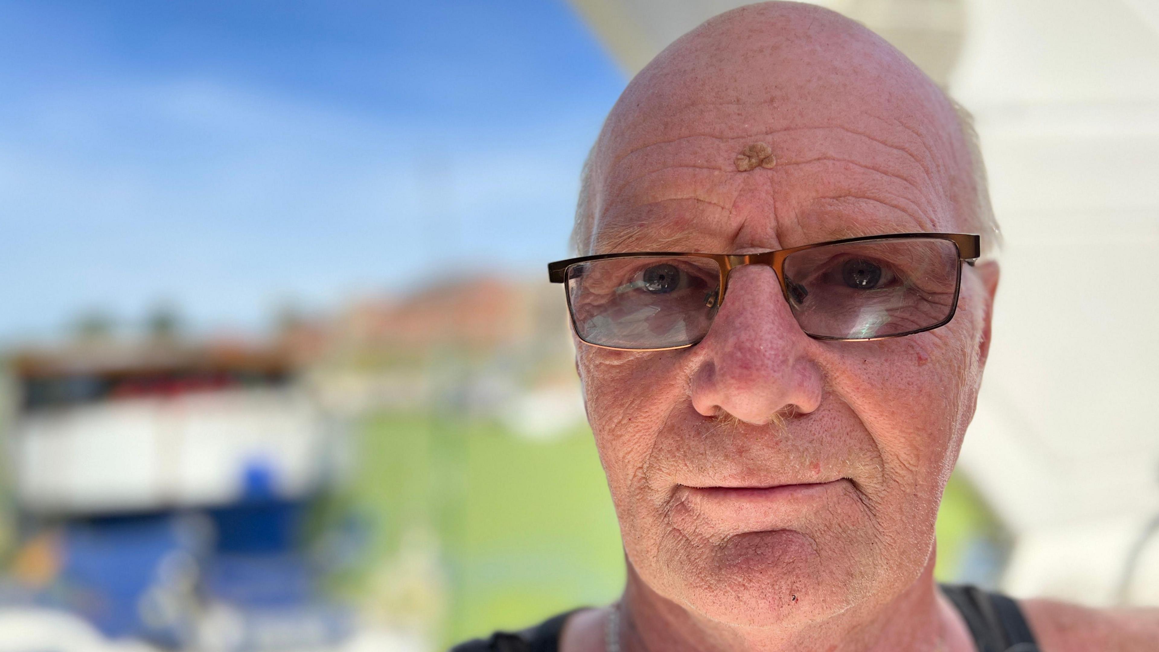 A close-up of Dave Bouttell on his boat with the river in the background. He has a serious expression and is wearing lightly tinted sunglasses