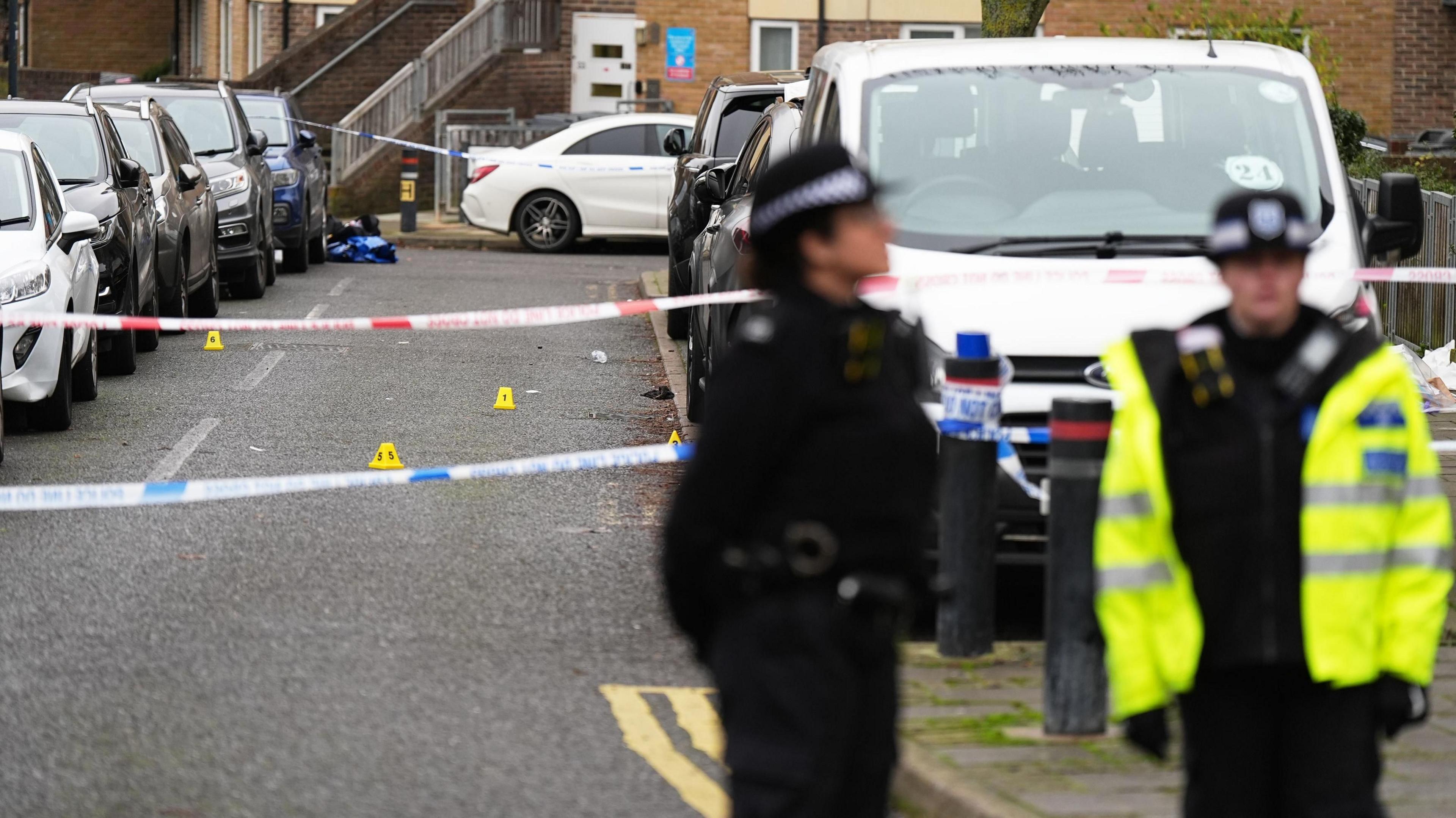 Two police officers stand on residential street in front of crime scene cordon