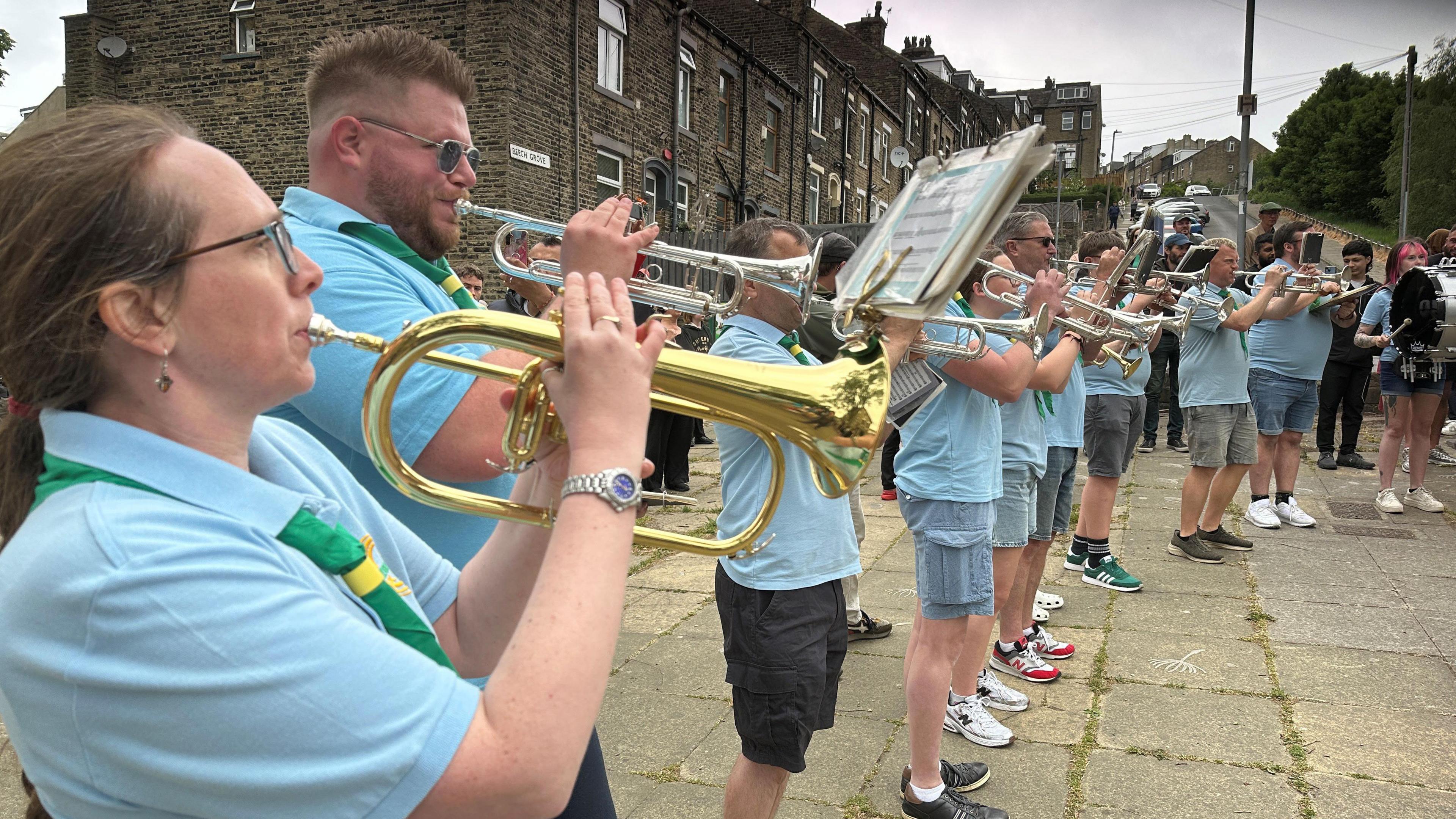 People all wearing blue polo shirts and a Scout neckerchief playing brass instruments