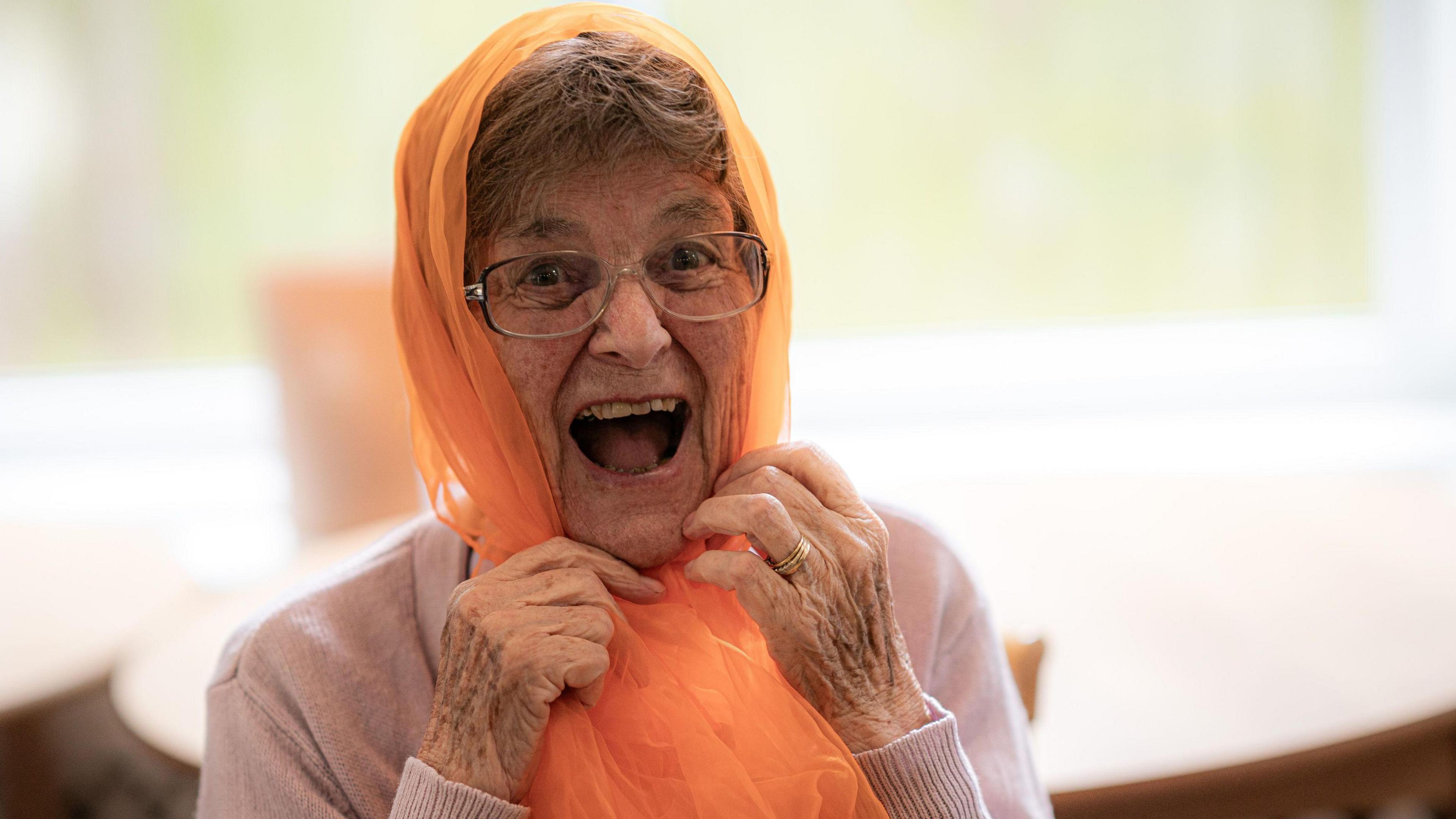 An older woman using a neon orange net as a headscarf and smiling.