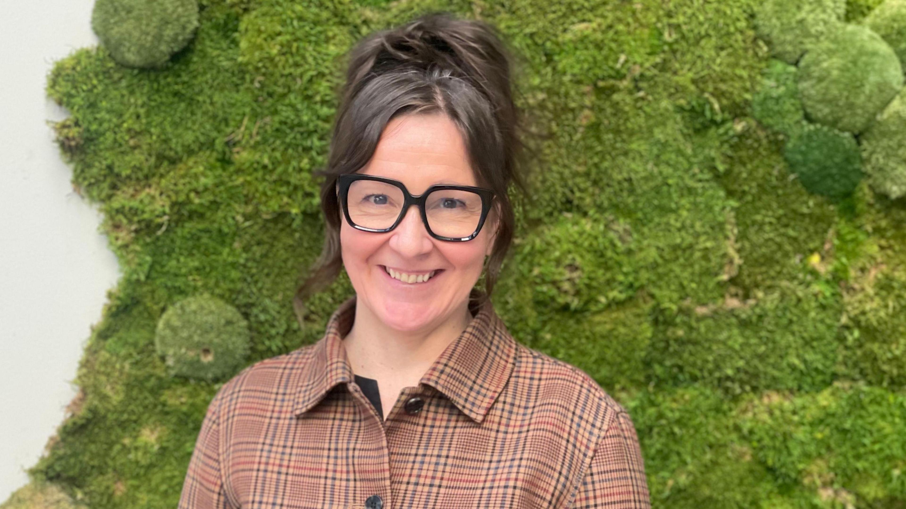 Jannie Jeppesen smiles at the camera, wearing a patterned top and thick framed, black glasses