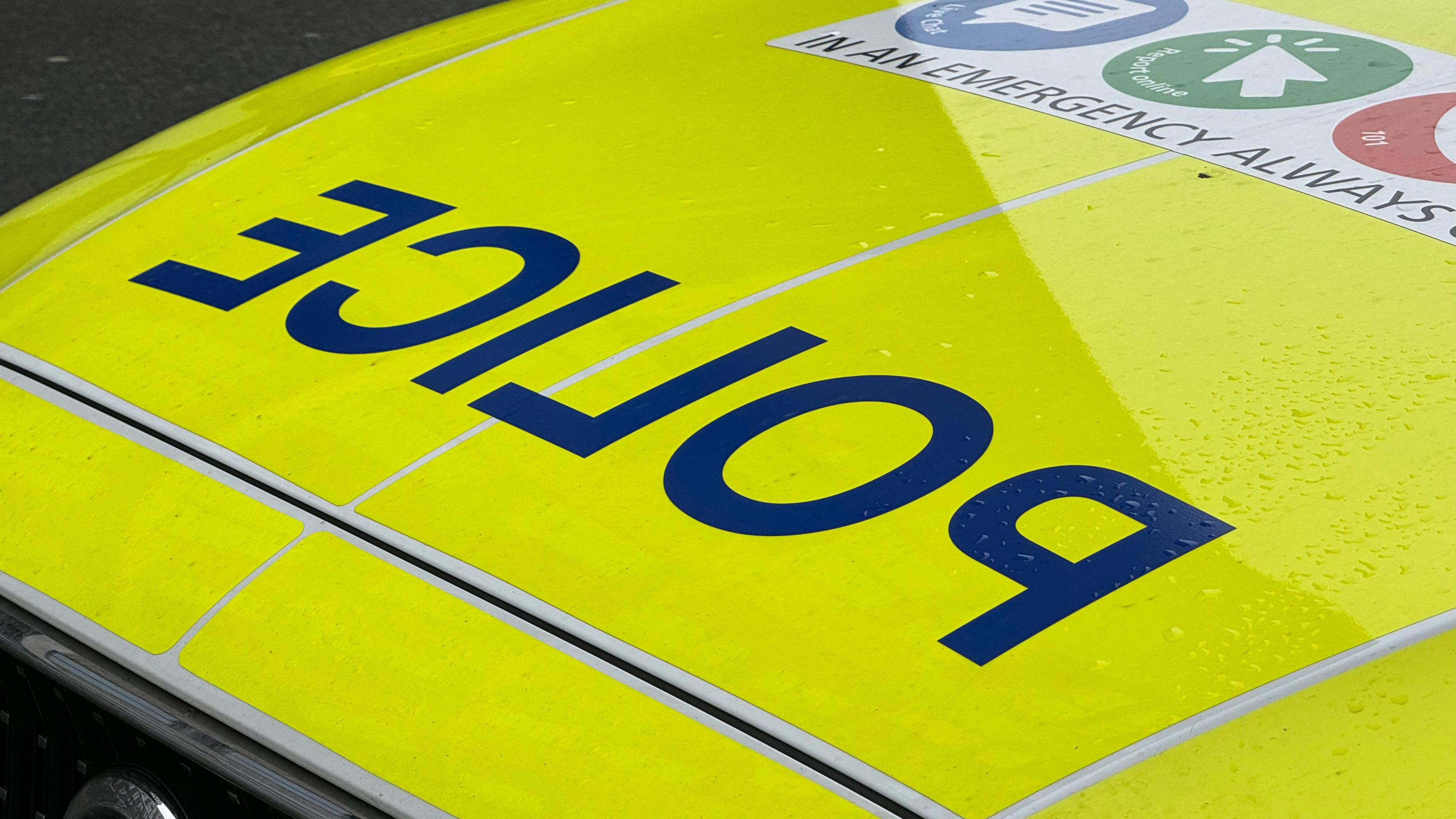 The fluorescent yellow bonnet of a car, with reversed lettering spelling the word police.