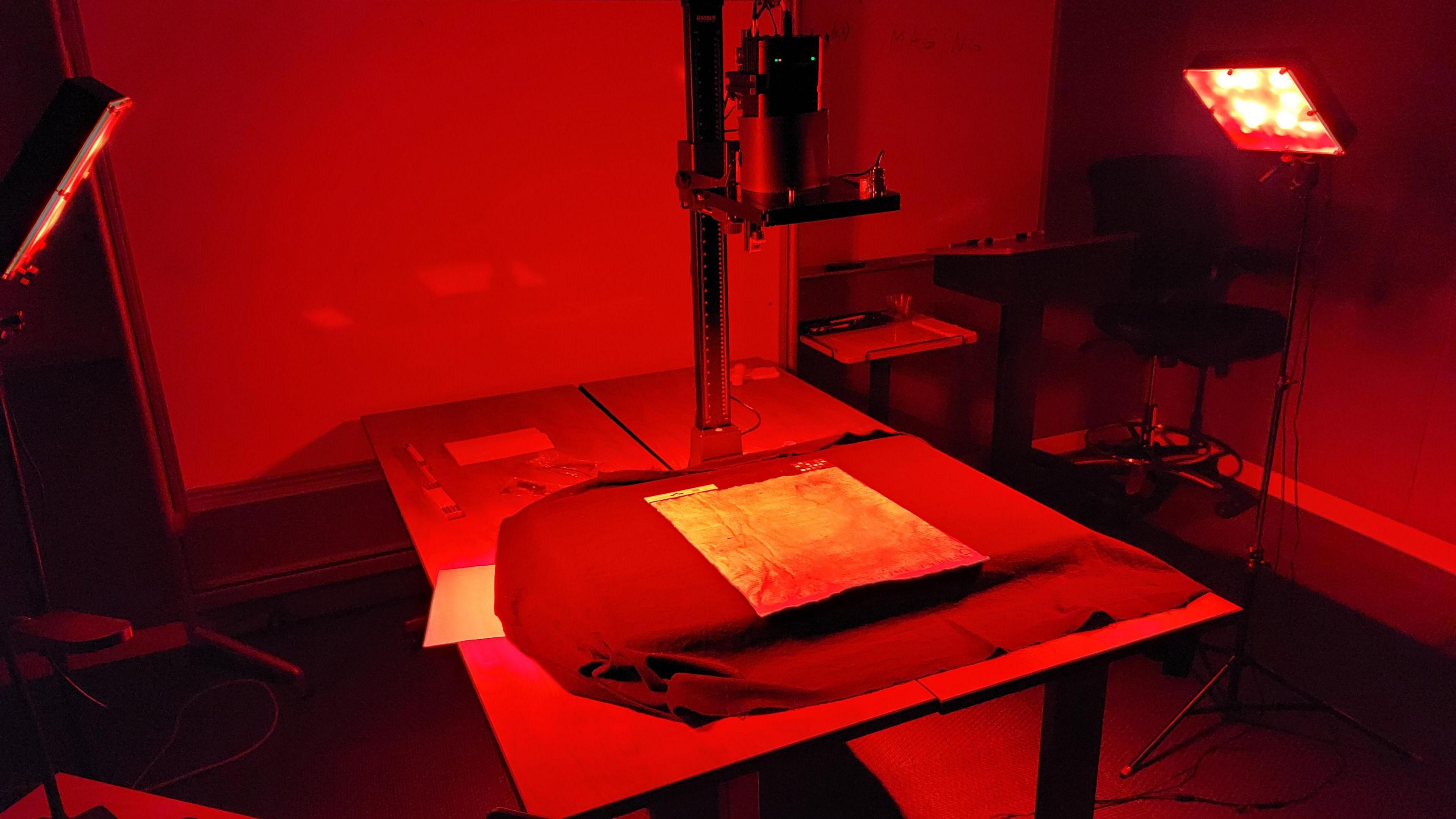 The Magna Carta sits on a table and the room is illuminated in red as lights focus on the document to check for its authenticity.