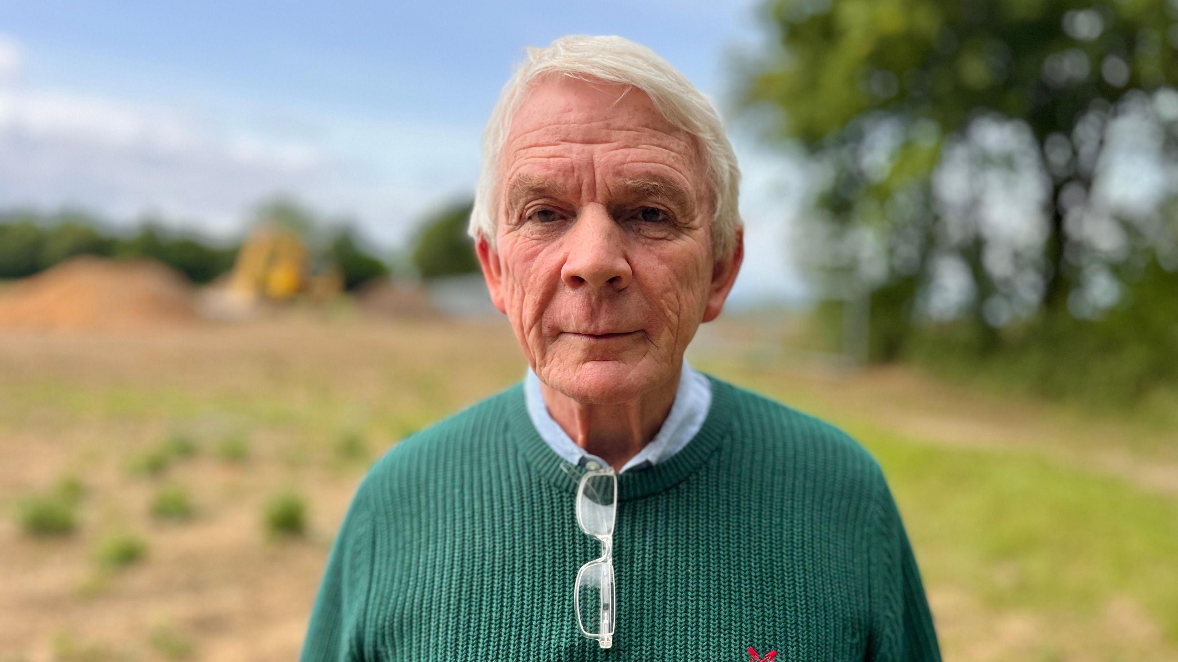 Farmer David Grant with white hair and wearing a green jumper, standing in a field