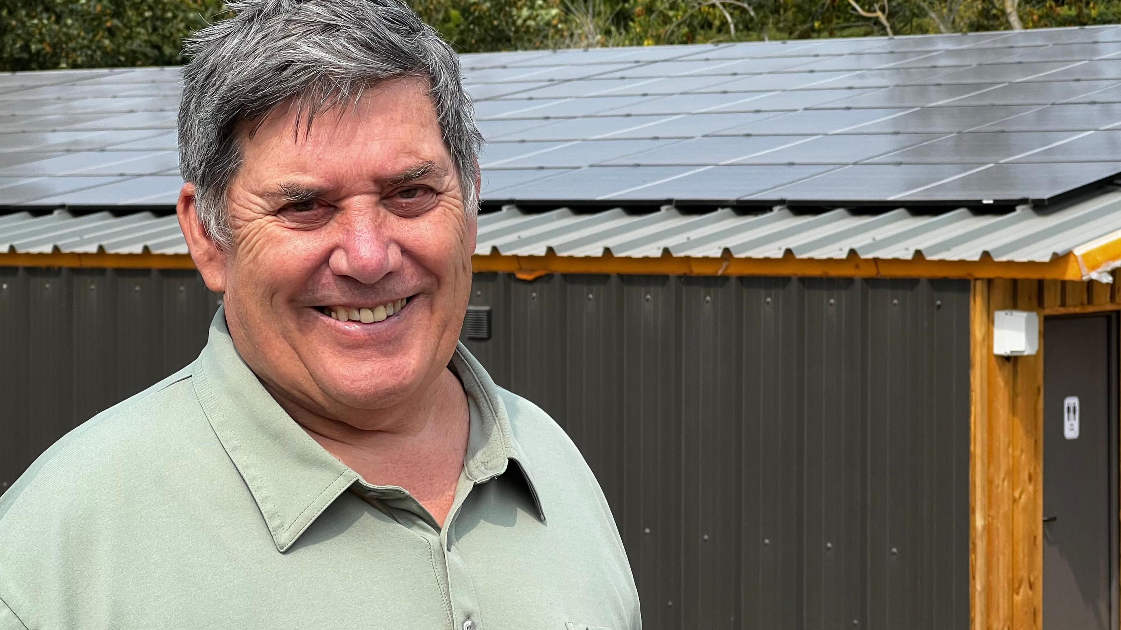 David Baker, smiling, in front of his dairy, with solar panels on the roof.