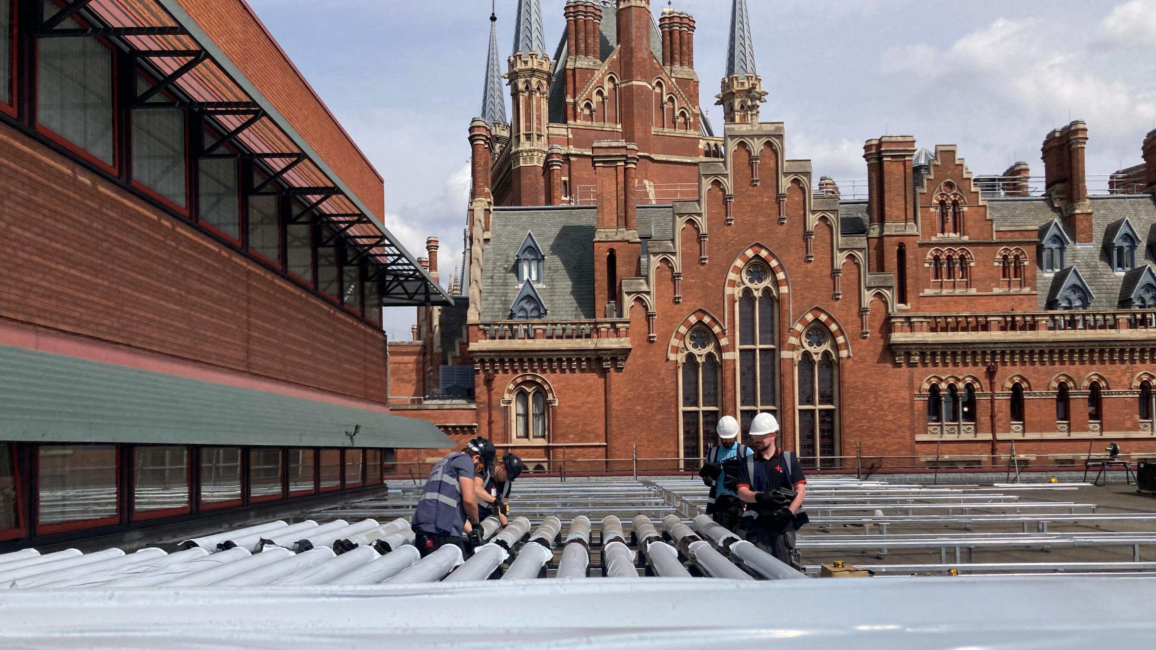 Four workers in hard hats and navy clothing install the solar technology on the roof of the building