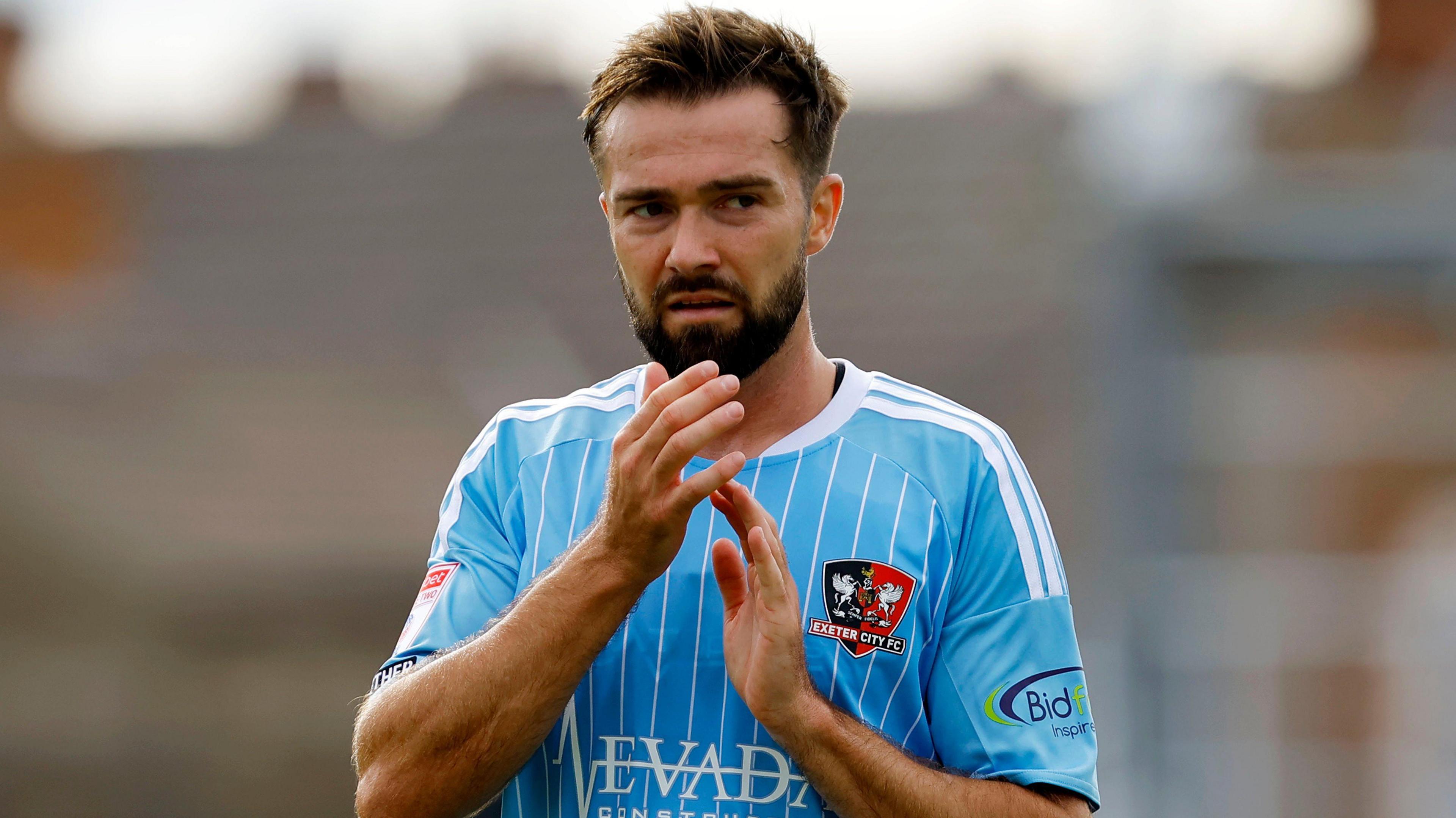 Gwion Edwards claps fans wearing light blue & thin white-striped away kit