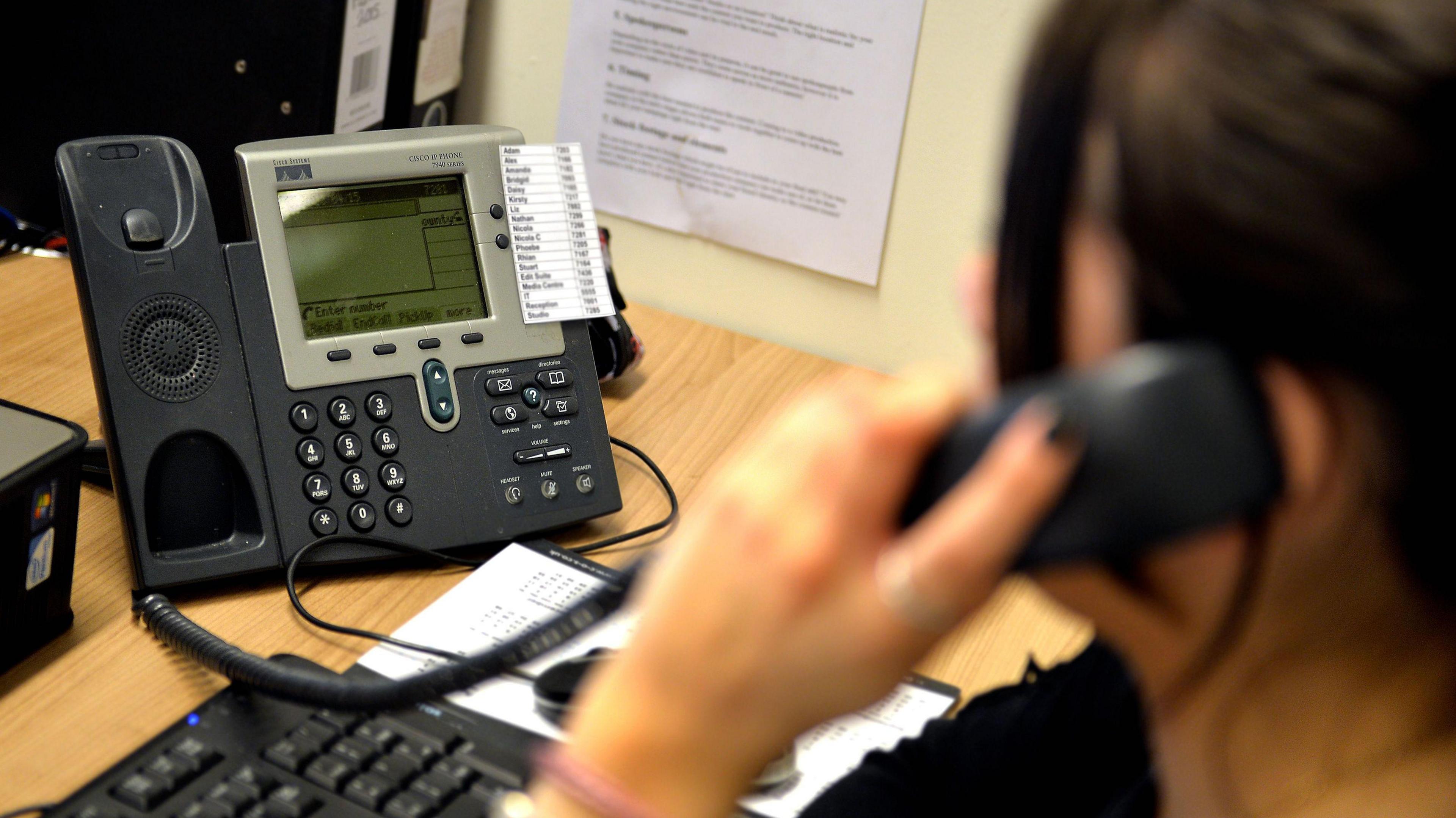 The back of a woman on the phone at her desk.