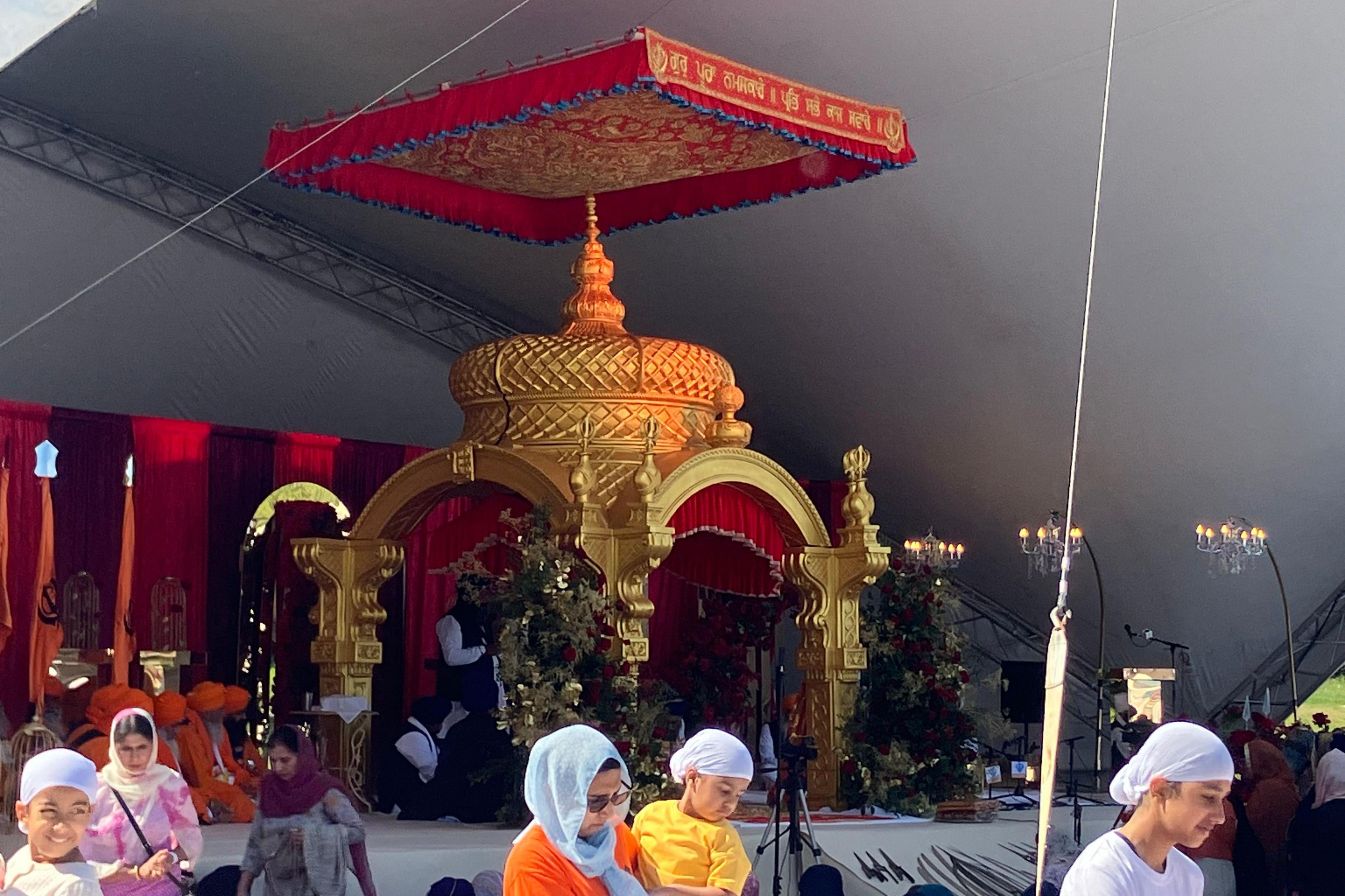 A large ornate golden monument on a stage. There are people in the foreground wearing white headscarves.