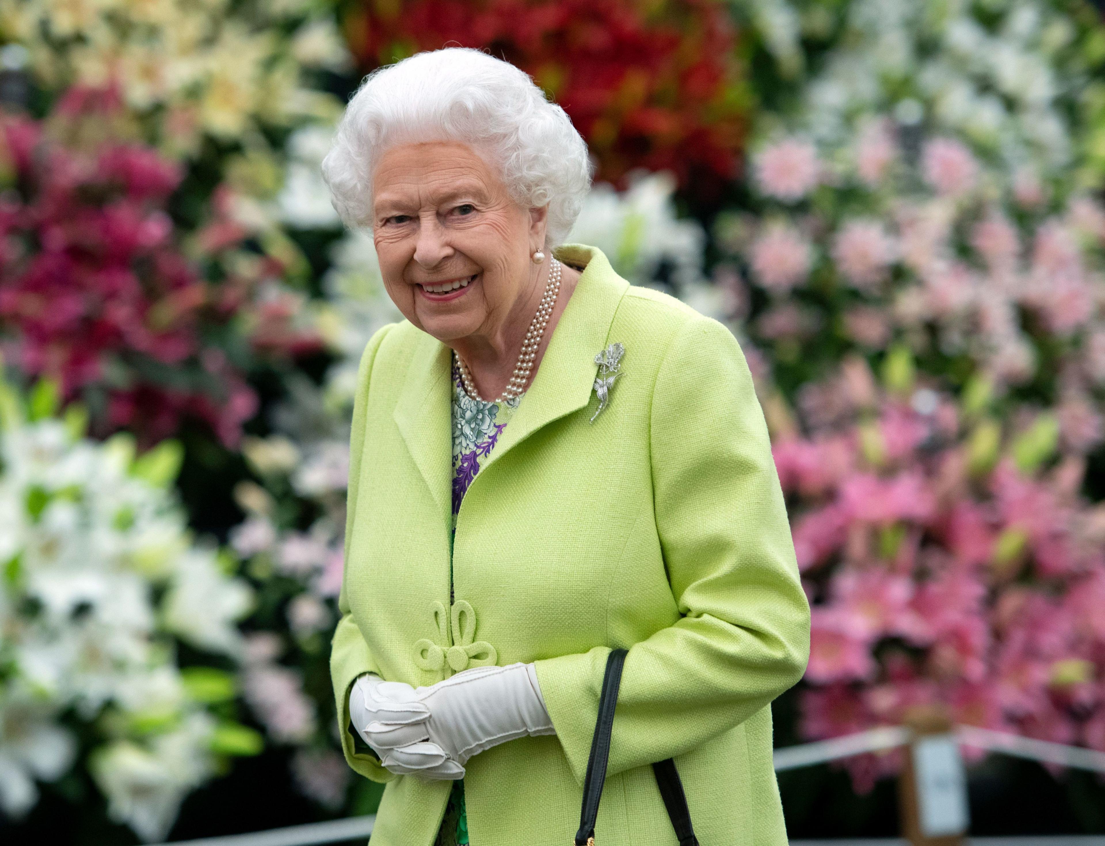 Elizabeth II wears a green jacket in front of a cornucopia of colourful flowers 