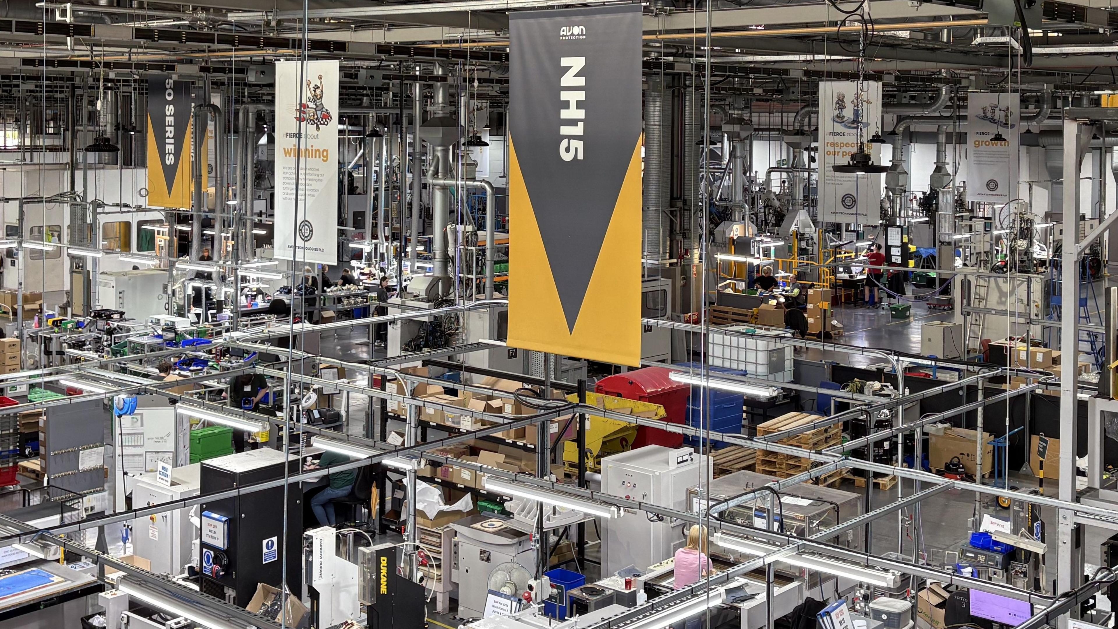The factory floor at the Avon Protection in Melksham, Wiltshire with banners hanging from the ceiling and multiple different units and production lines.