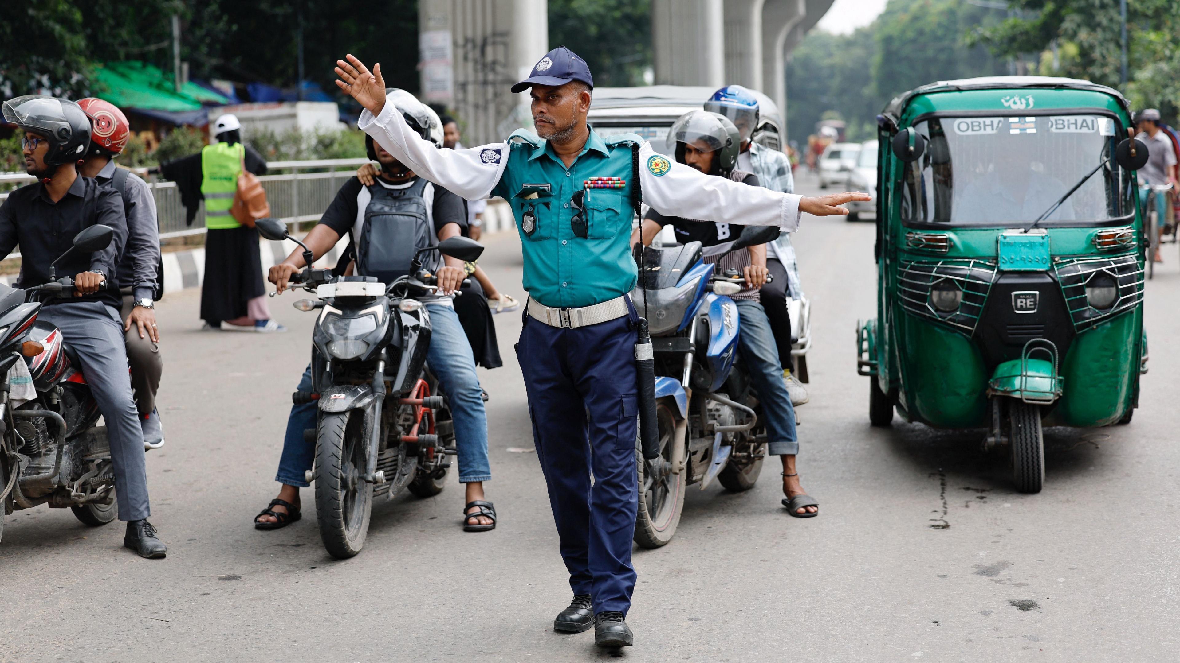 A traffic police officer gestures to the vehicles at an intersection in Dhaka