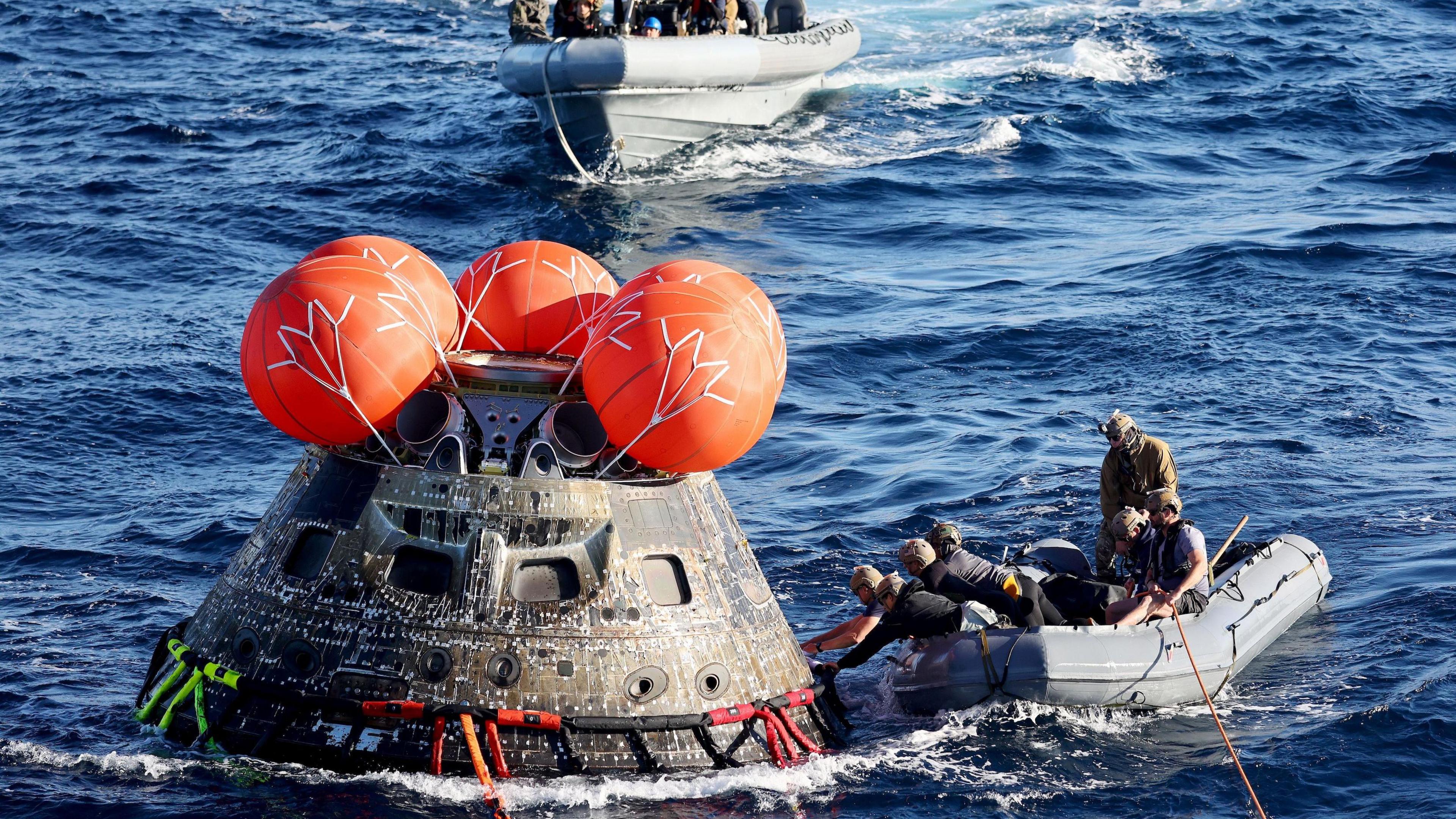 a spacecraft with red balls on top of it - to its right, a speedboat with people coming to collect it