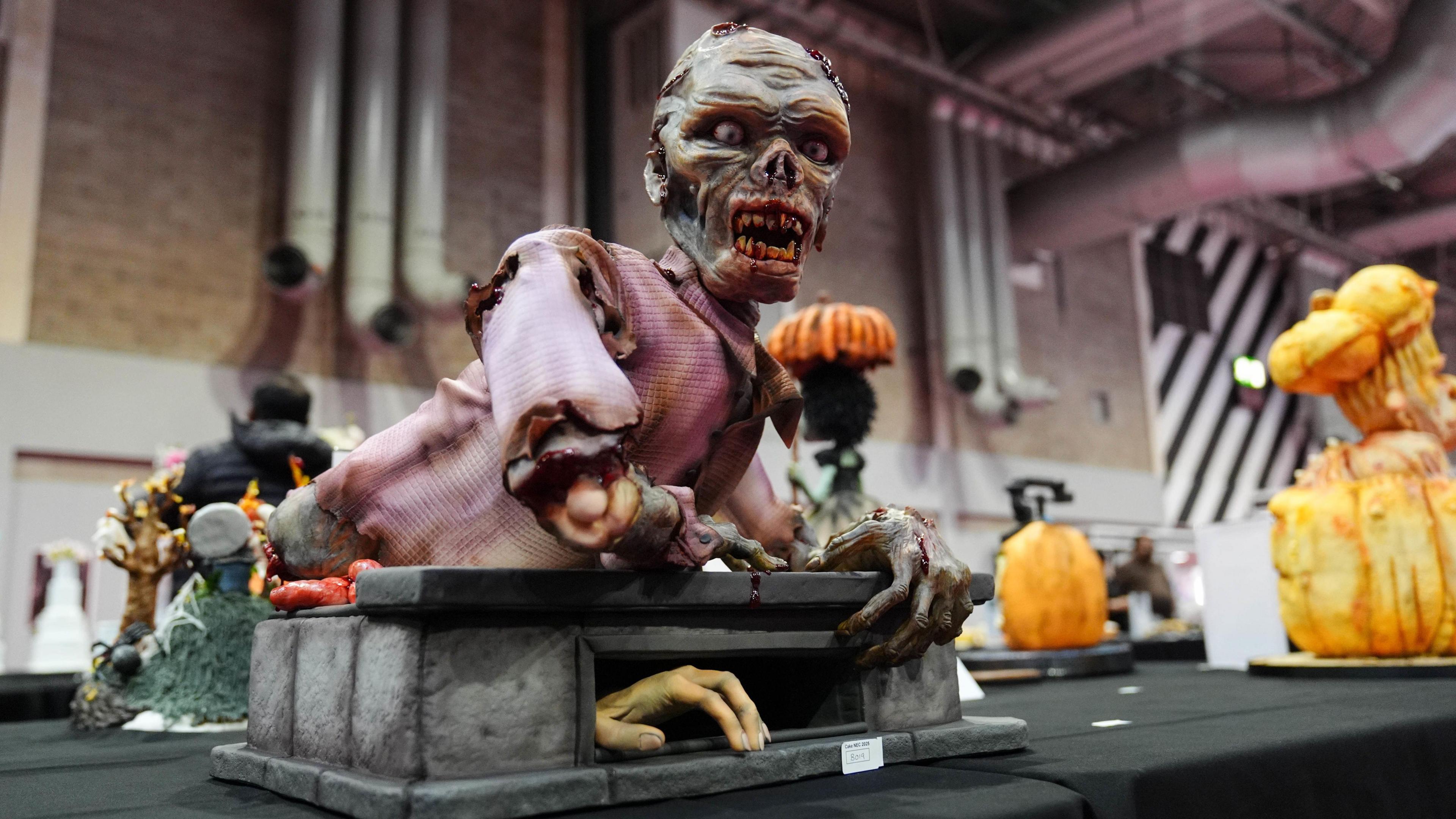 A cake display showing a dismembered, skeletal figure, whose upper body has been placed on a small plinth. A hand can be seen creeping out of a hole at the front.