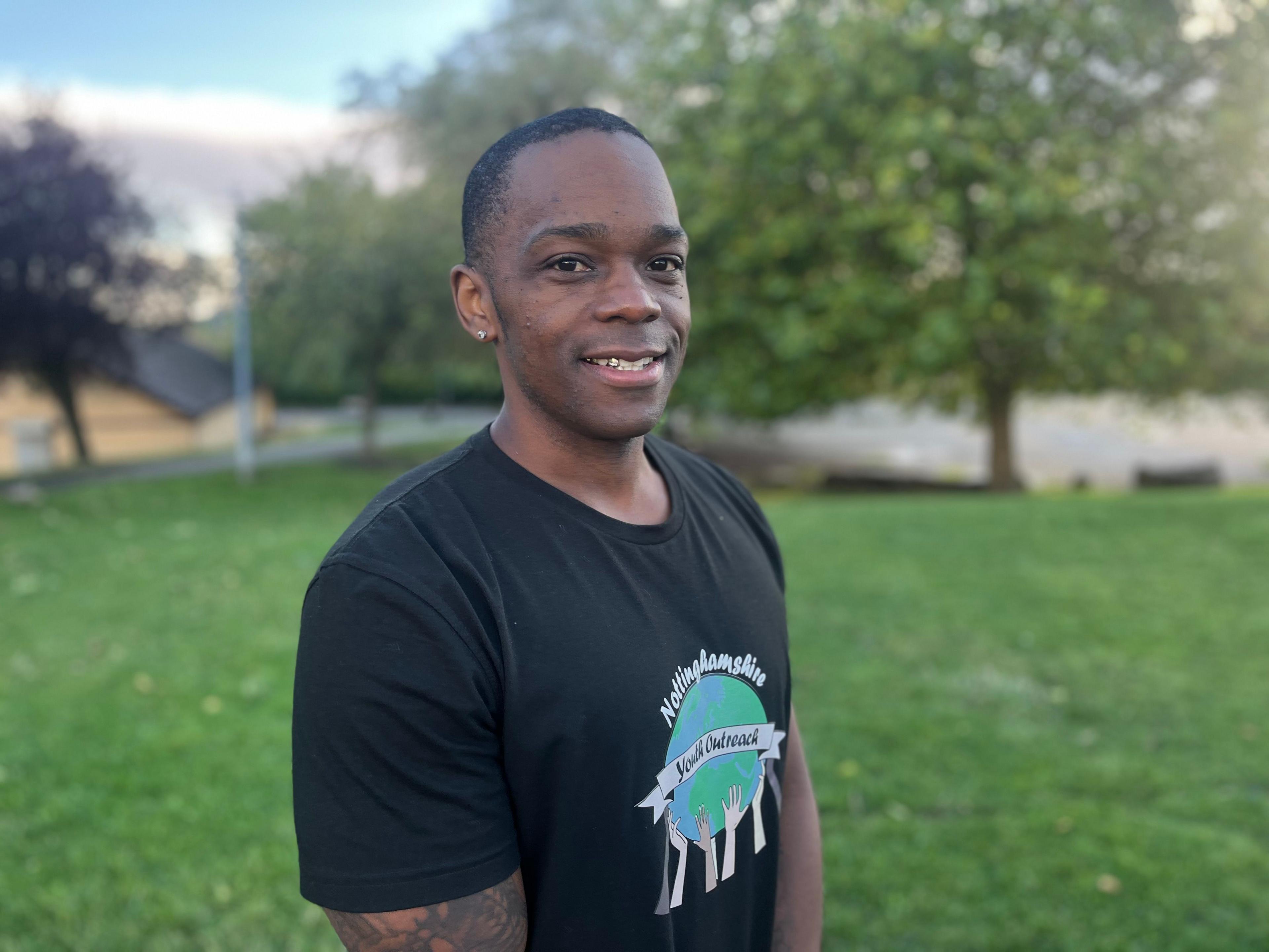 Romel Davis pictured outside the youth club in Bilborough while smiling. He is wearing a black shirt.