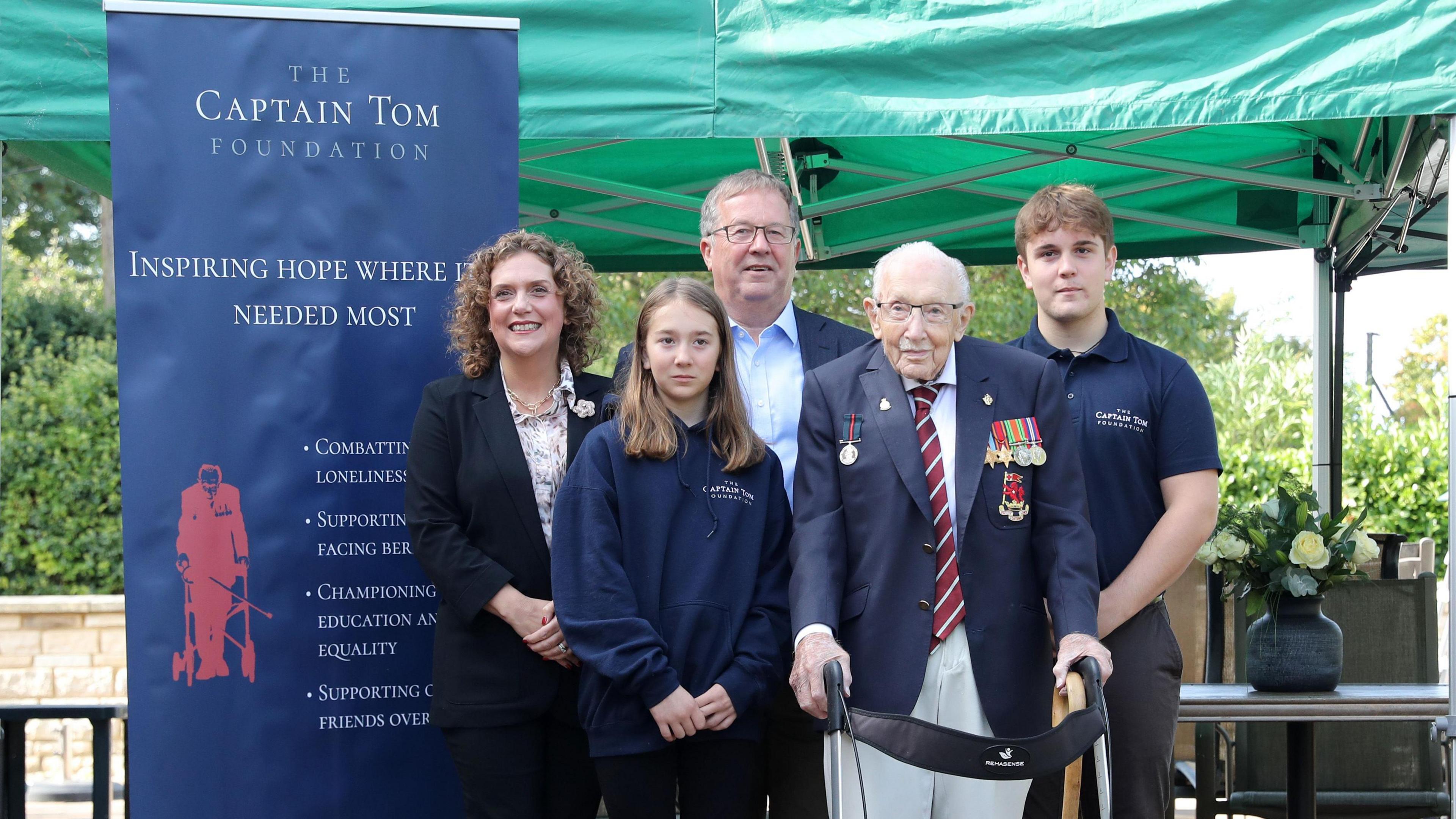 Captain Sir Tom Moore standing with a walking frame with his family