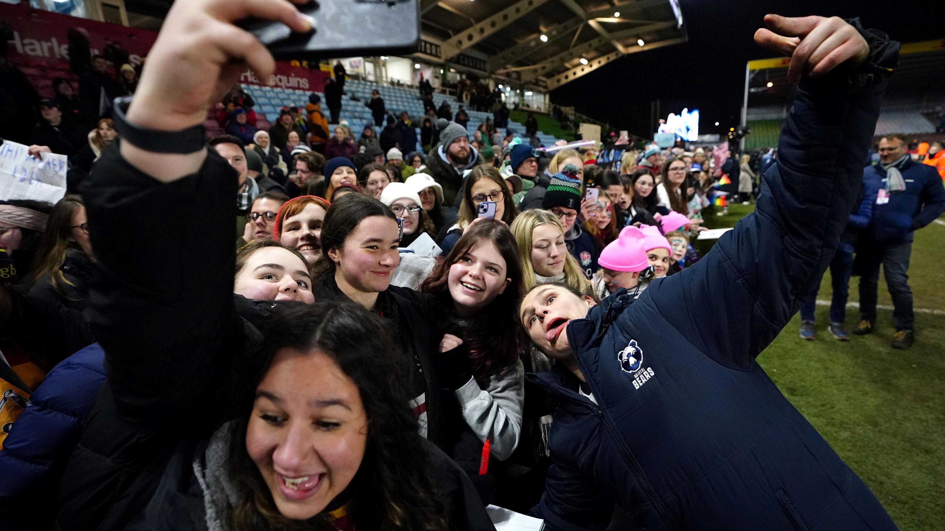 Bristol Bears rugby player Ilona Maher pulls a funny face, sticking out her tongue, as she leans in close to fans at the Twickenham Stoop after Bristol beat Harlequins women. The majority of the fans crowding into the selfie are young women