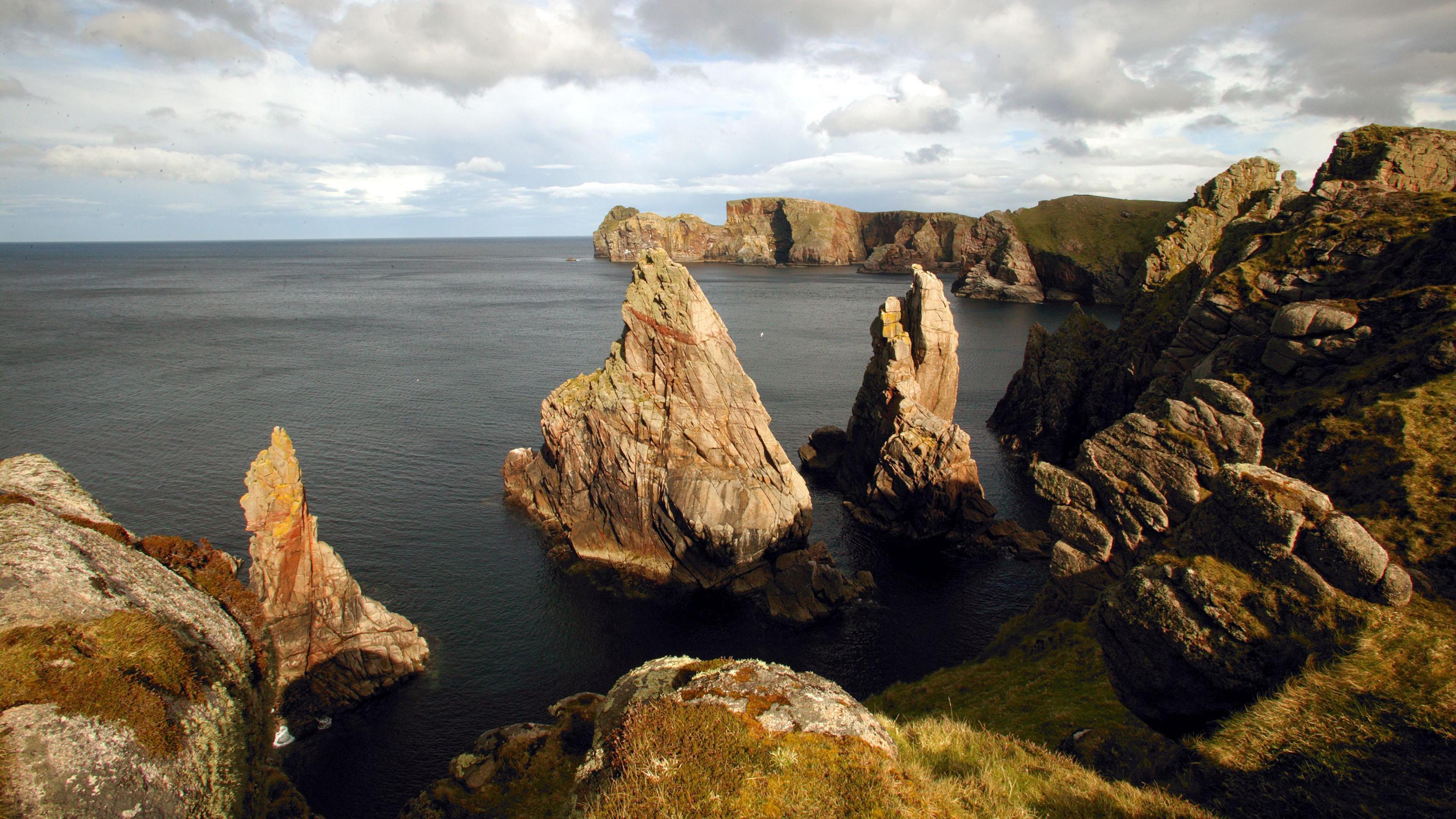 A stock image of Tory Island coastline - there are rocks emerging from the water, there is grass on the coastline.