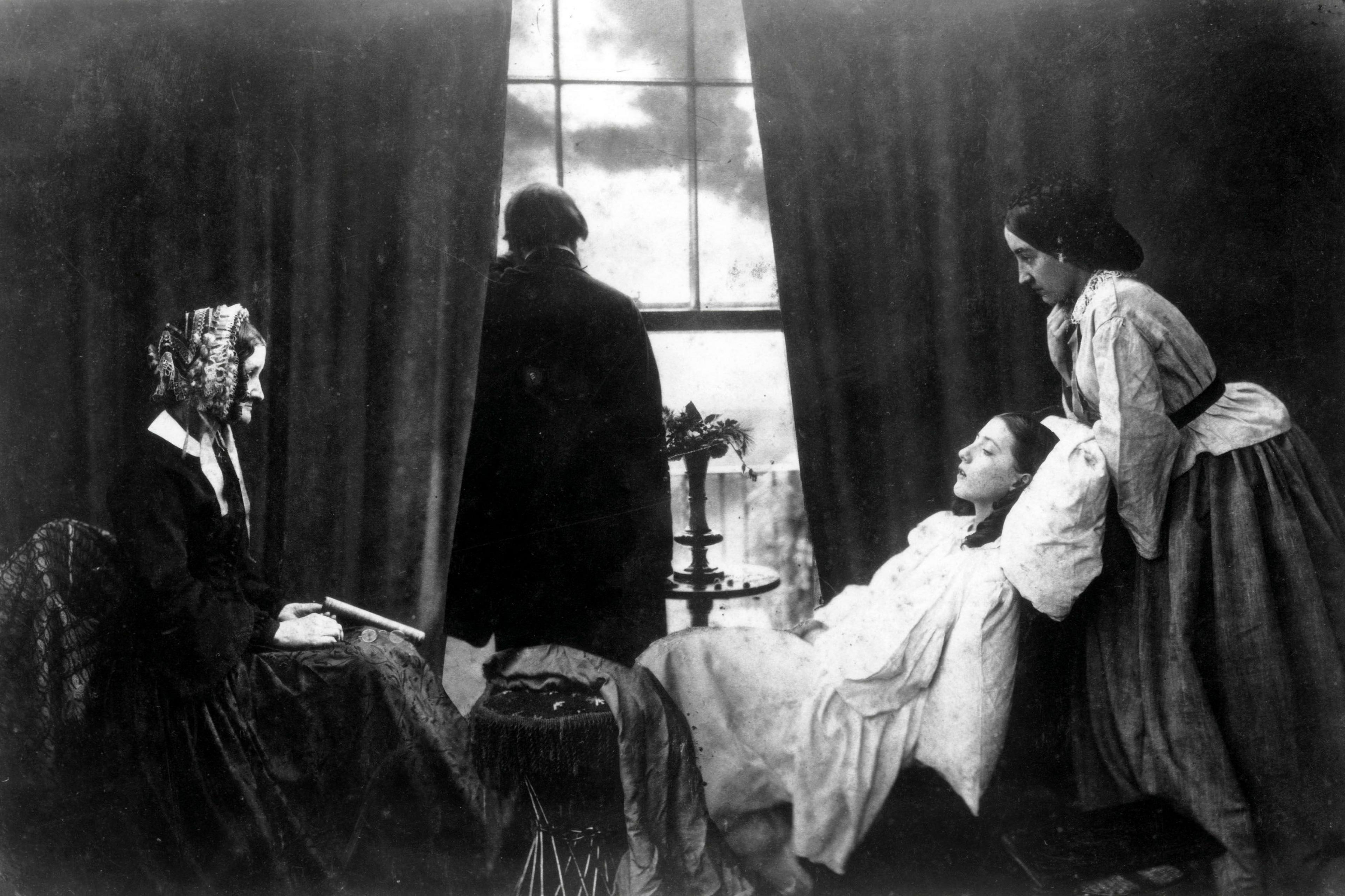 A young woman is seen on her death bed with two female members of her family, one at the foot and one at the head of her bed. A man stares out of a window in the background.