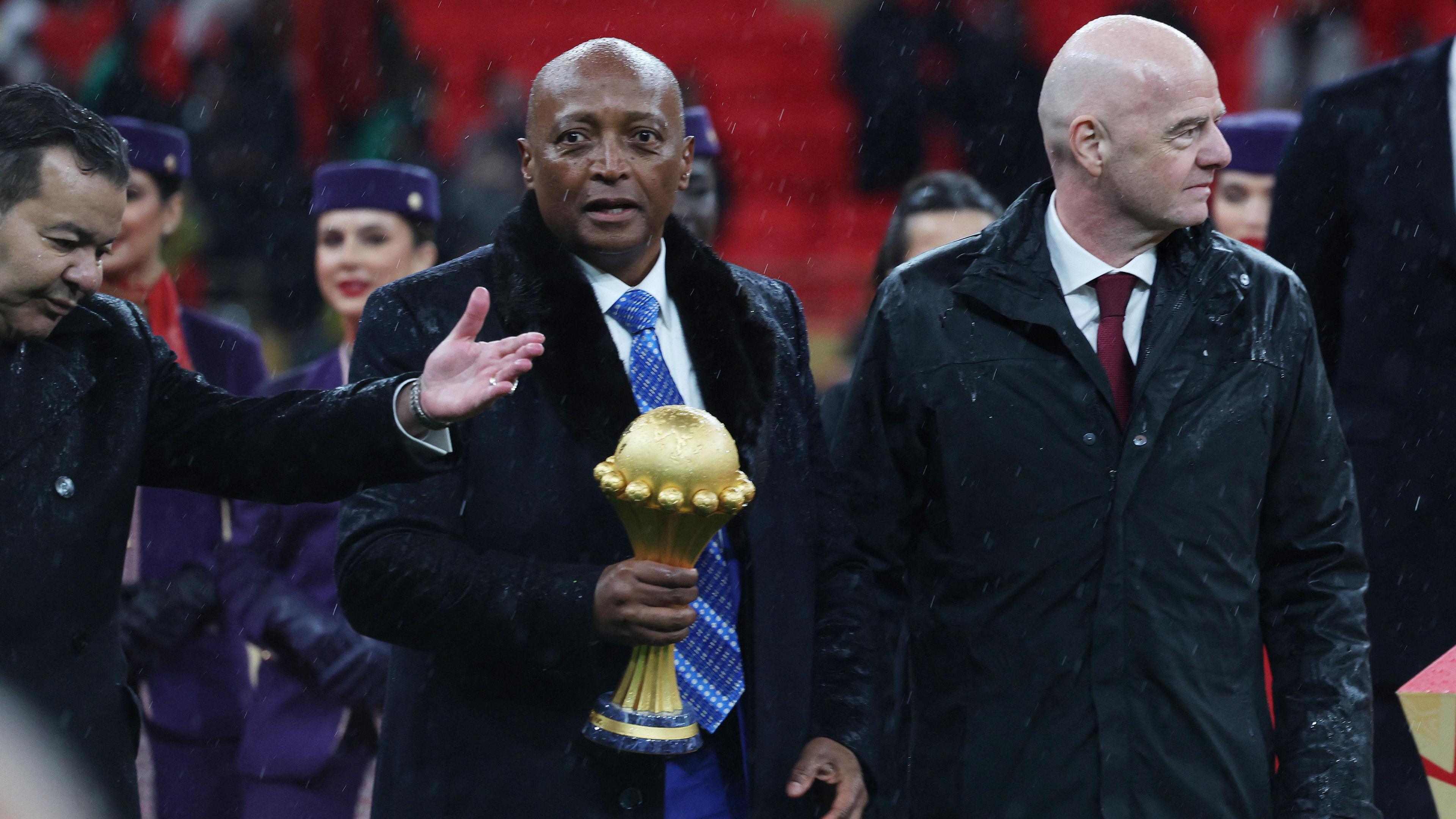 Caf president Patrice Motsepe, centre and dressed in a long black coat and white shirt and blue tie, carries the Africa Cup of Nations trophy in his right hand as he walks flanked by Fifa president Gianni Infantino.