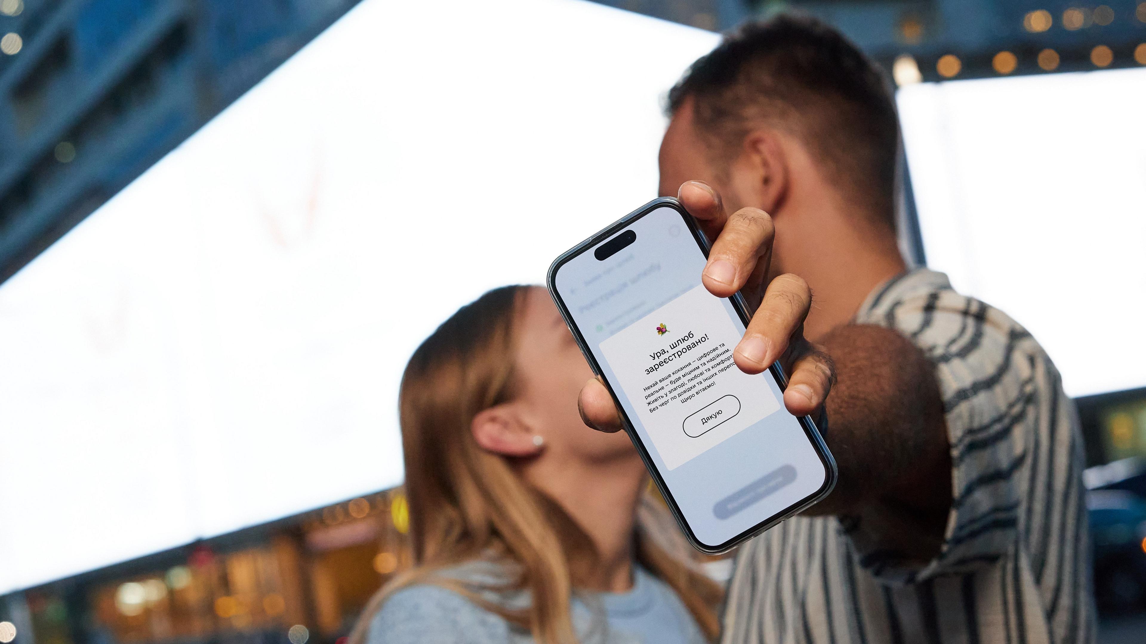 A couple appear to be kissing but one blocks the view with a phone showing the Diia app
