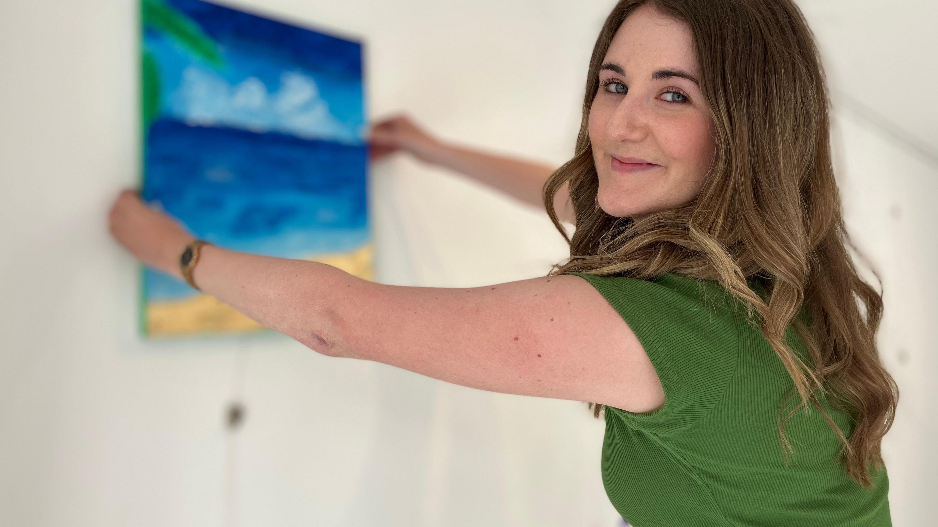 Megan Pilcher is hanging a painting on a white wall