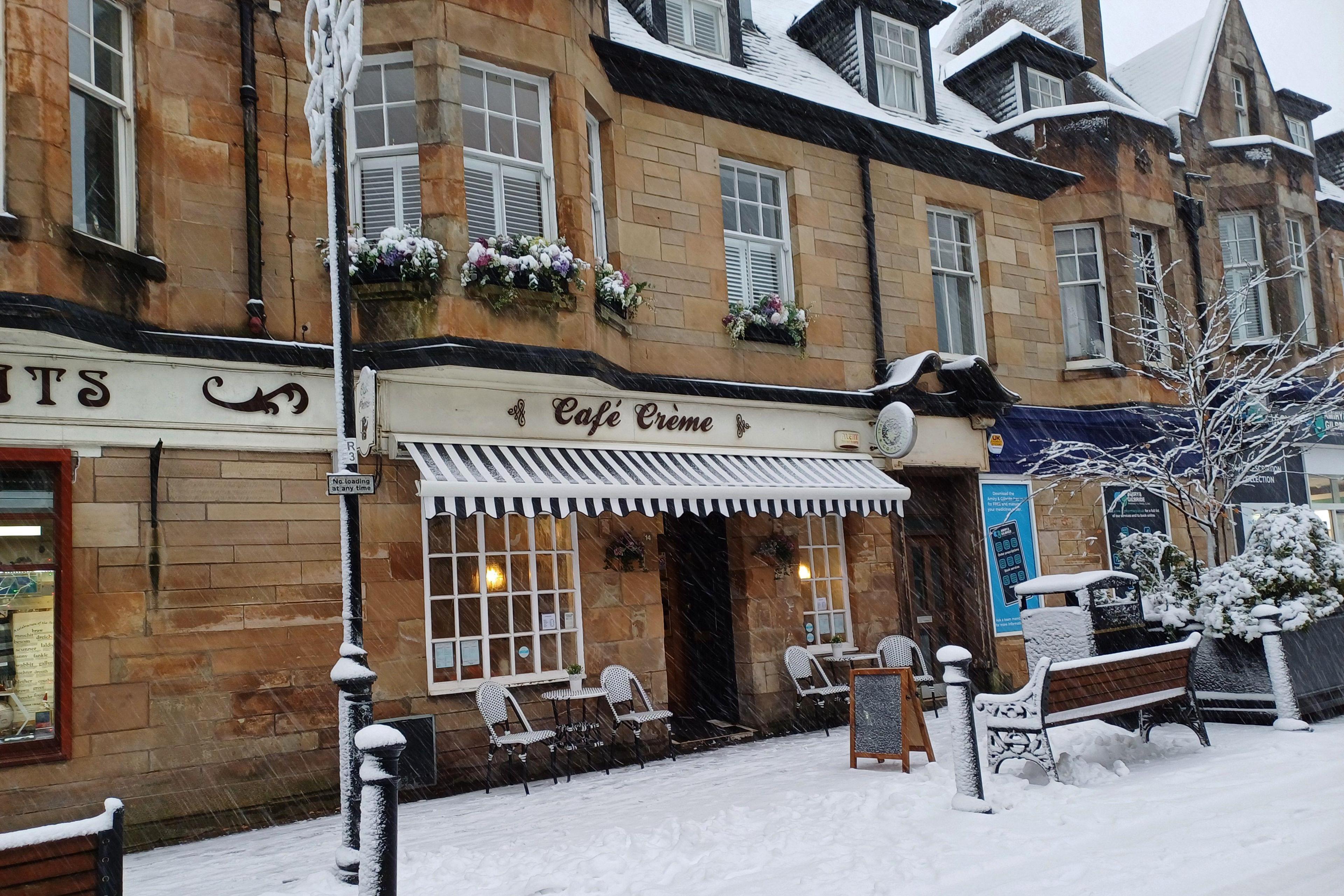 There are tables and chairs covered in snow outside a cafe building.