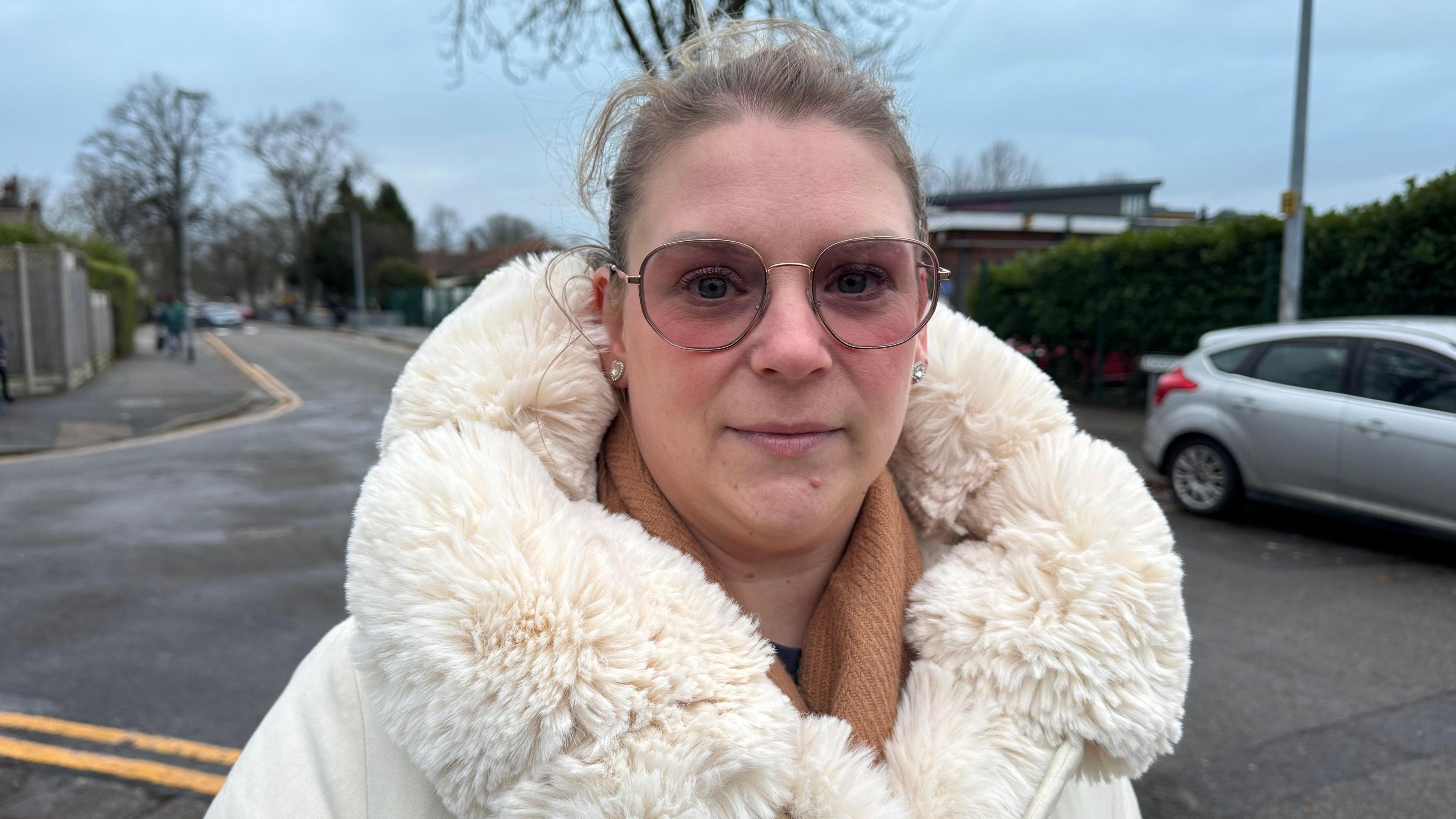 Stacey Talbot looks into the camera. She is wearing a cream fur coat and has tinted glasses.