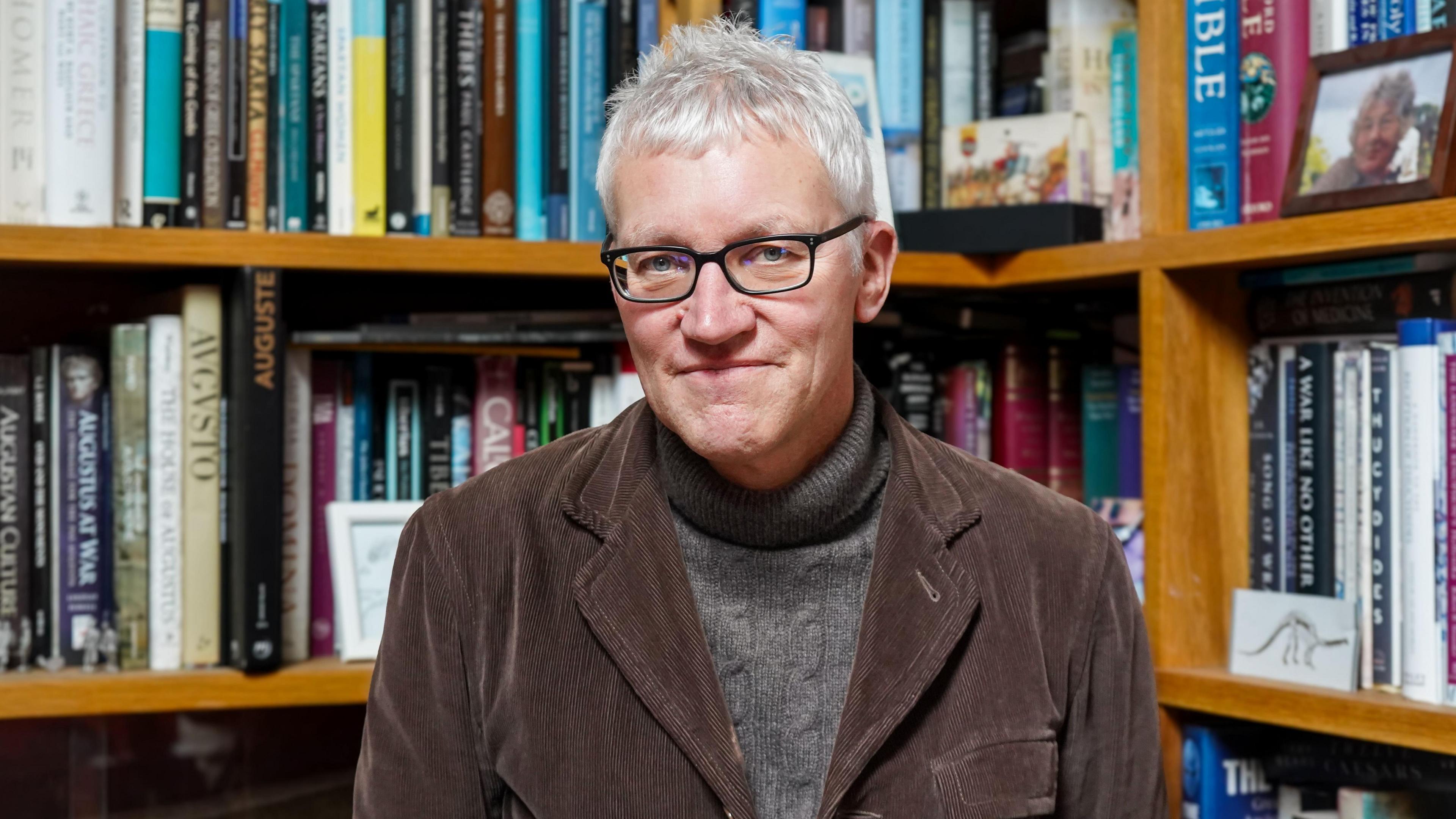 A man in a brown tweed jacket with glasses on.