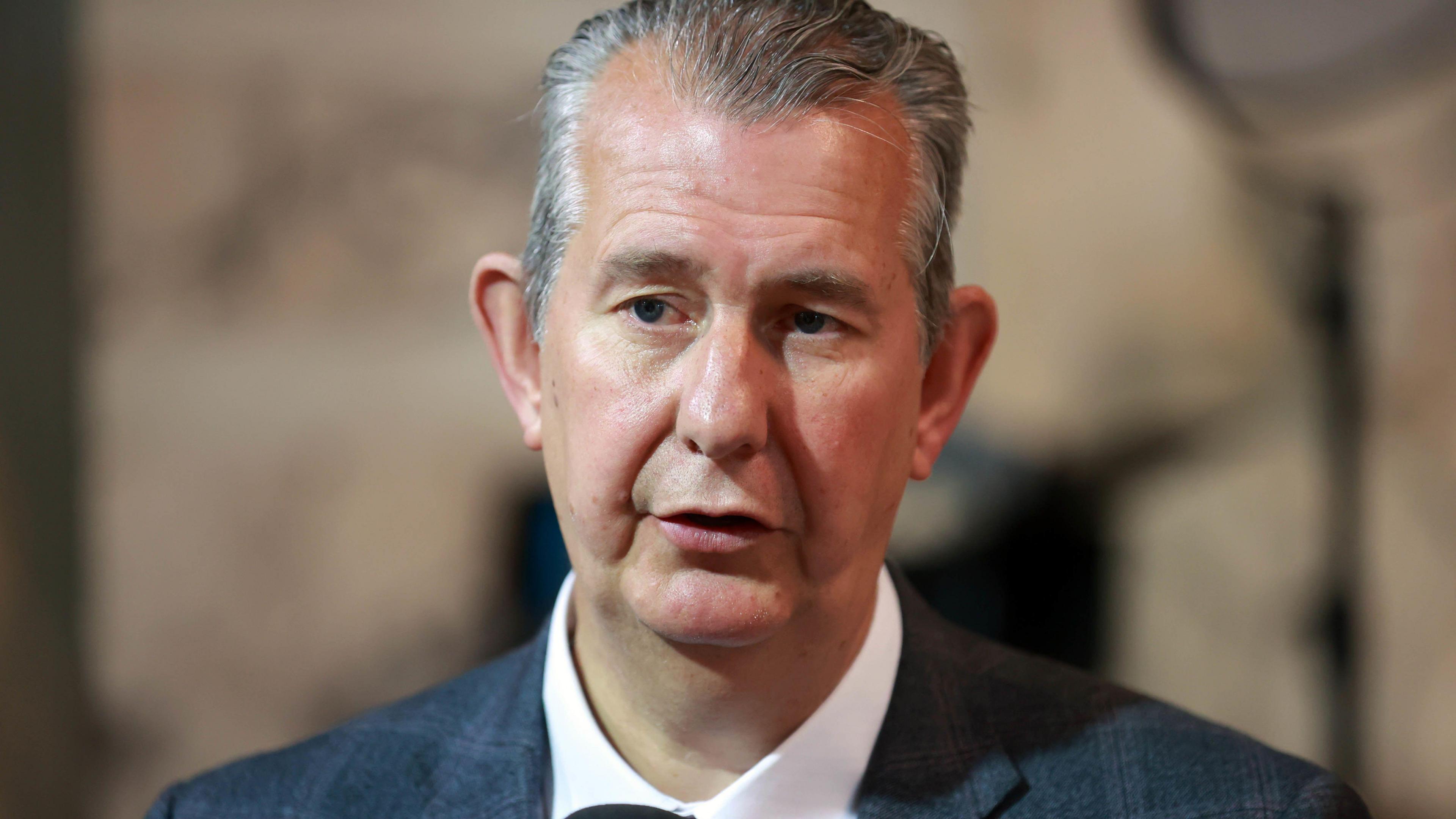 Headshot of Edwin Poots speaking. He is wearing a suit. The background is out of focus.