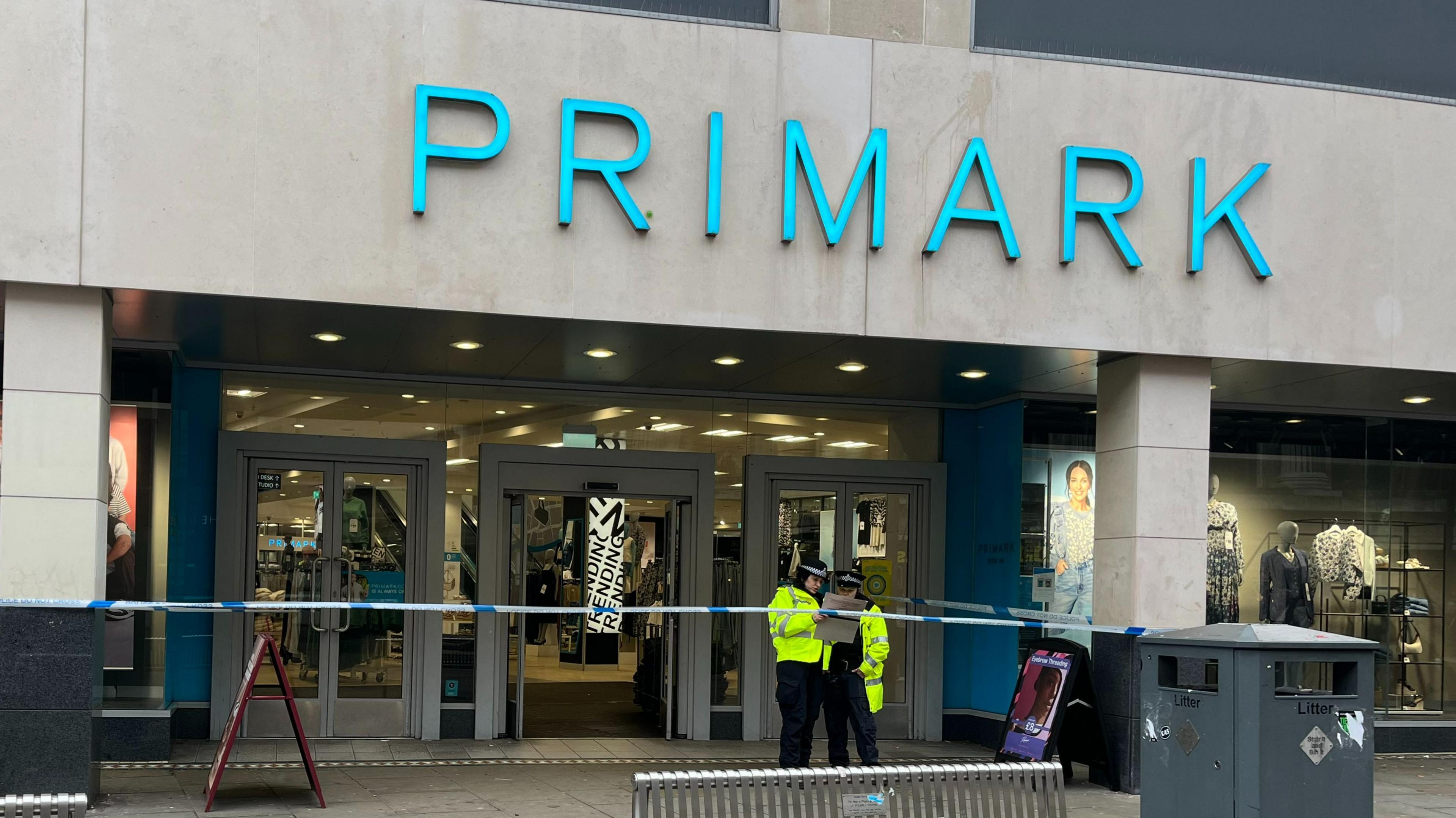 Two police officers in hi-vis jackets stand behind a police cordon outside the main entrance to Nottingham's Primark.