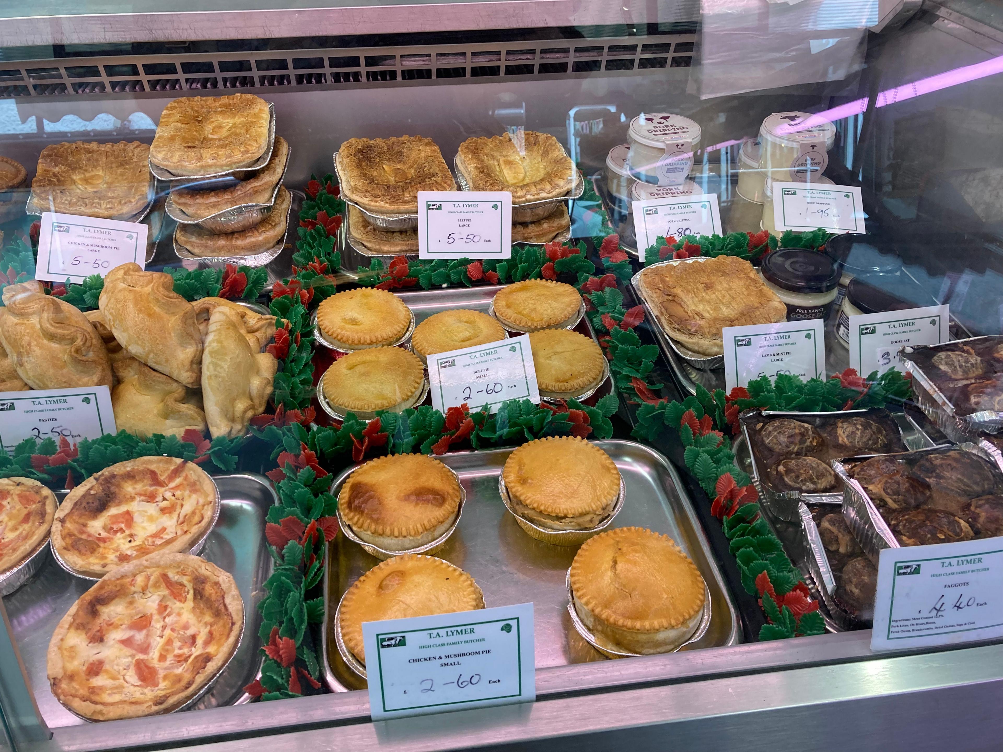 A glass cabinet containing food that includes meat pies, pasties and faggots.