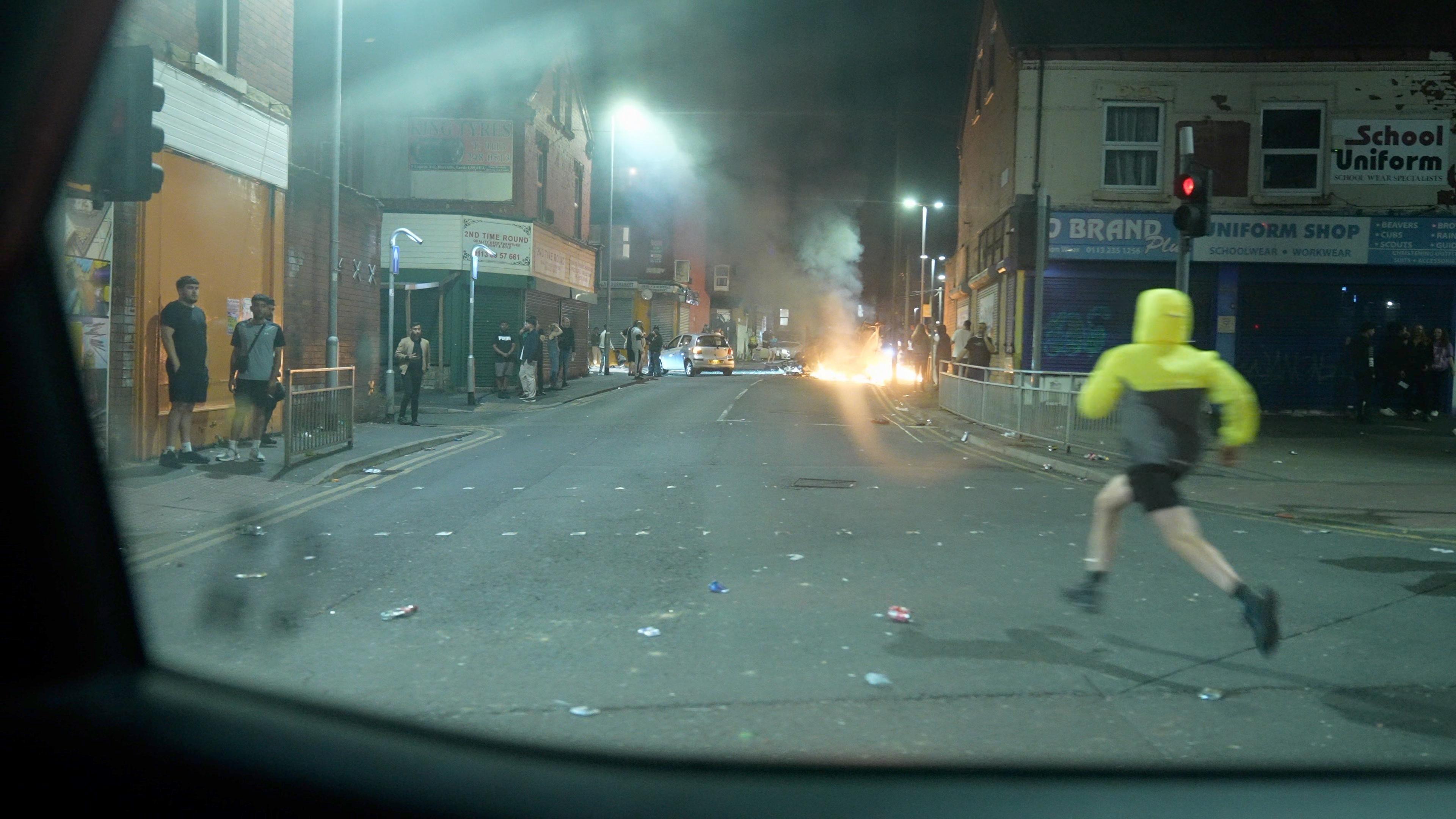 A man running through the street in Harehills as a bus burns in the distance