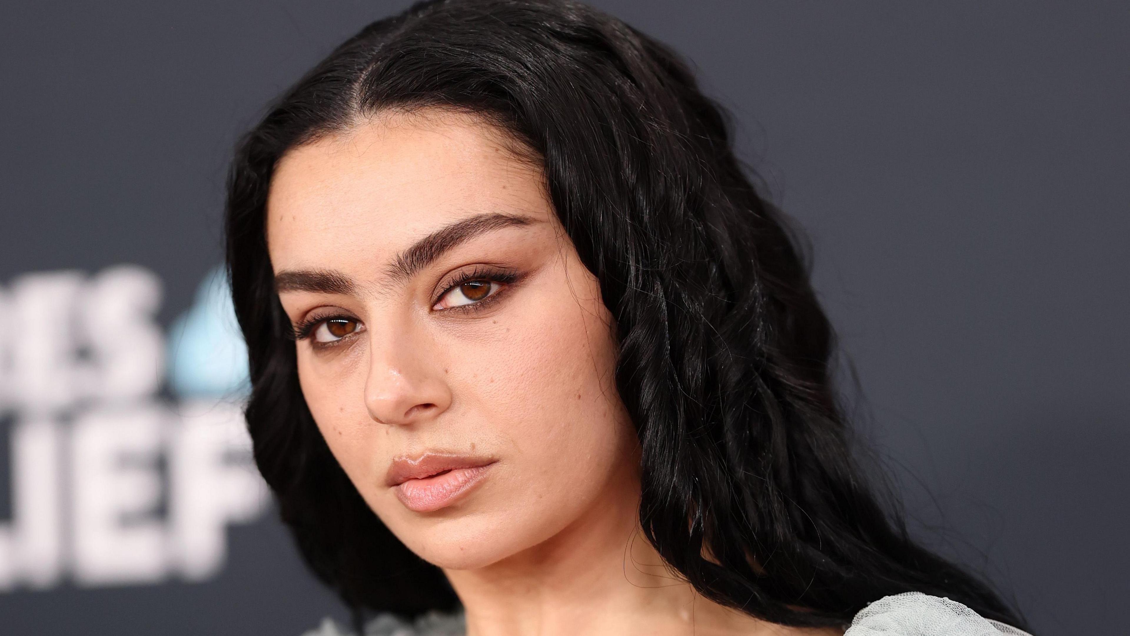 Charli XCX in a grey chiffon dress poses for photographers on a red carpet