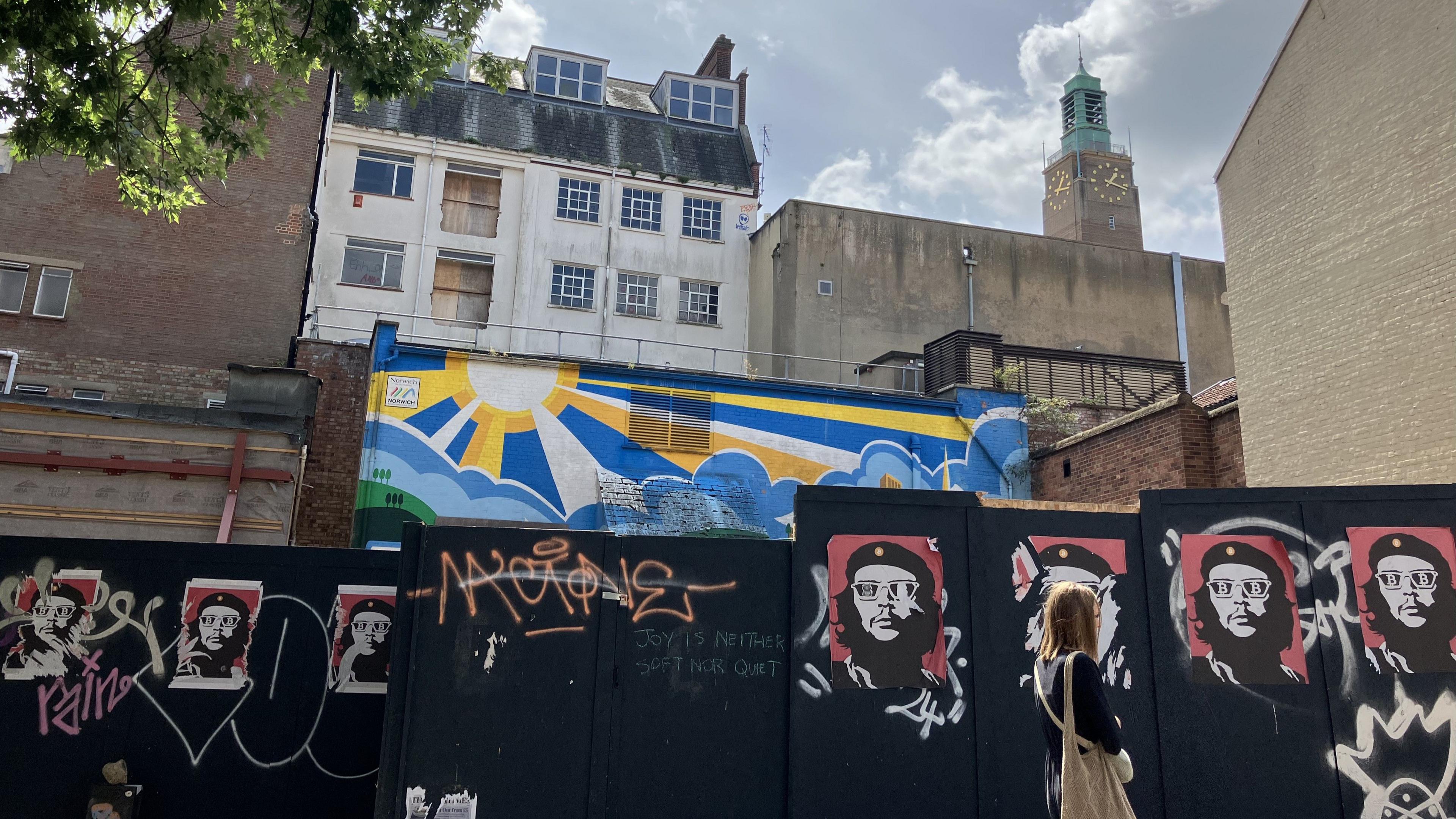 A partly-demolished four-storey building is shown in a disused state with posters and graffiti plastered on its external fencing.