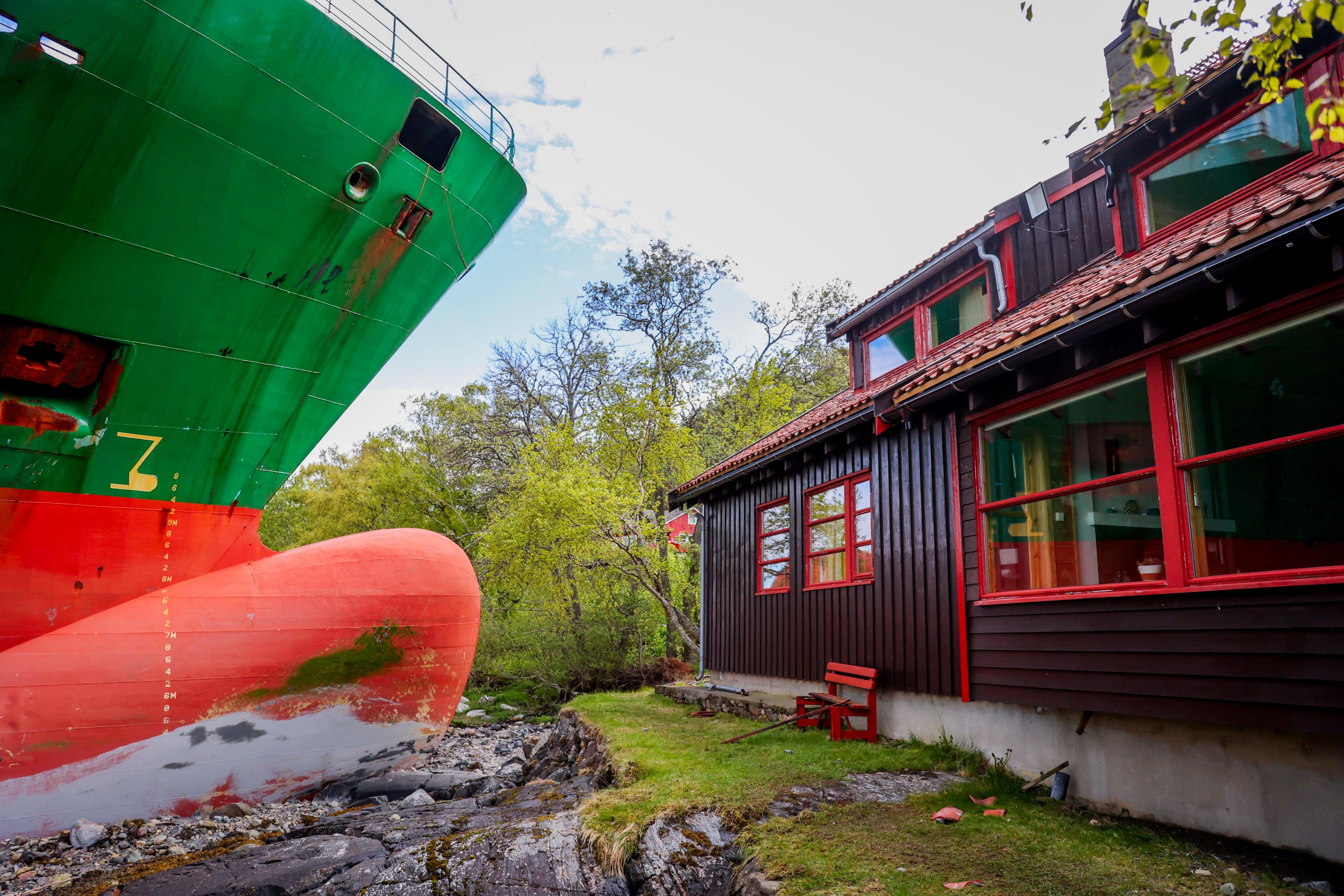 the profile of the nose of a brightly coloured ship stuck on rocks with a house sat just a few metres away