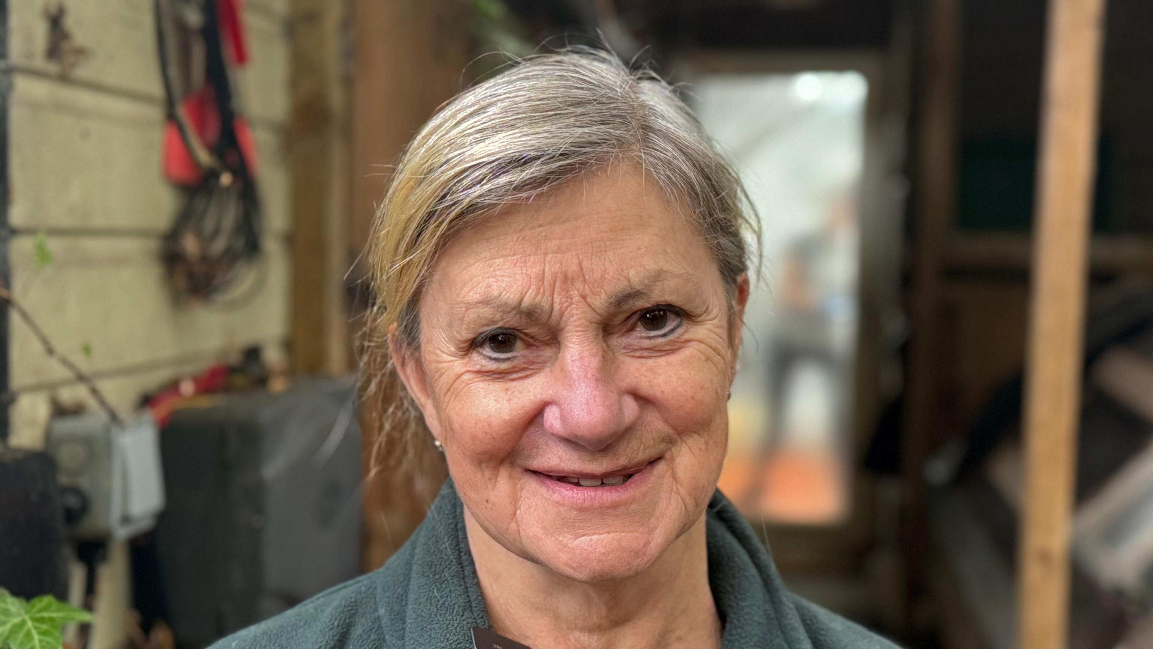 A head and shoulders image of Sue Stubley standing outside while wearing a green sweater. She is smiling and looking into the camera.