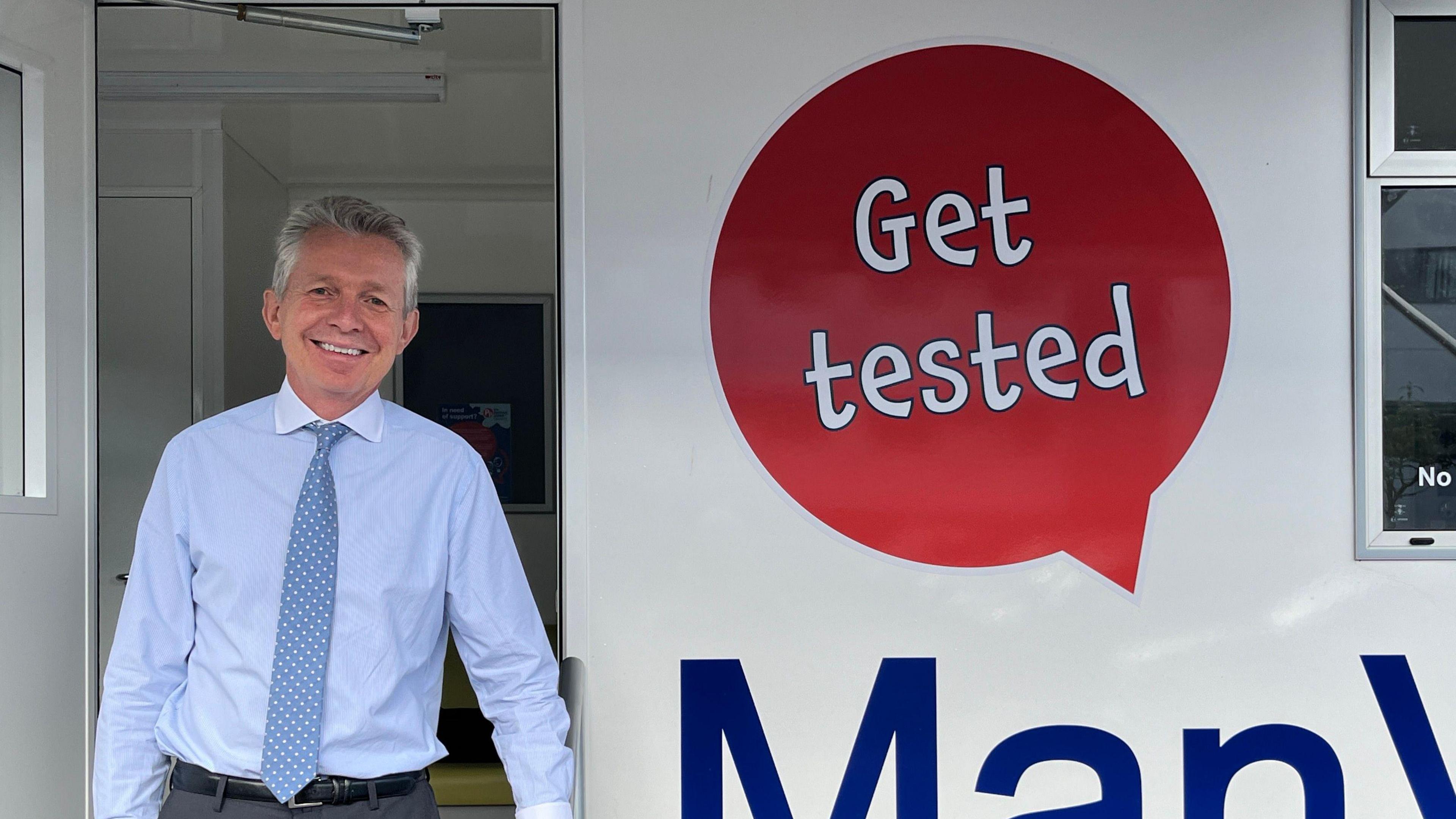 A man in a shirt and tie stands in front of a van