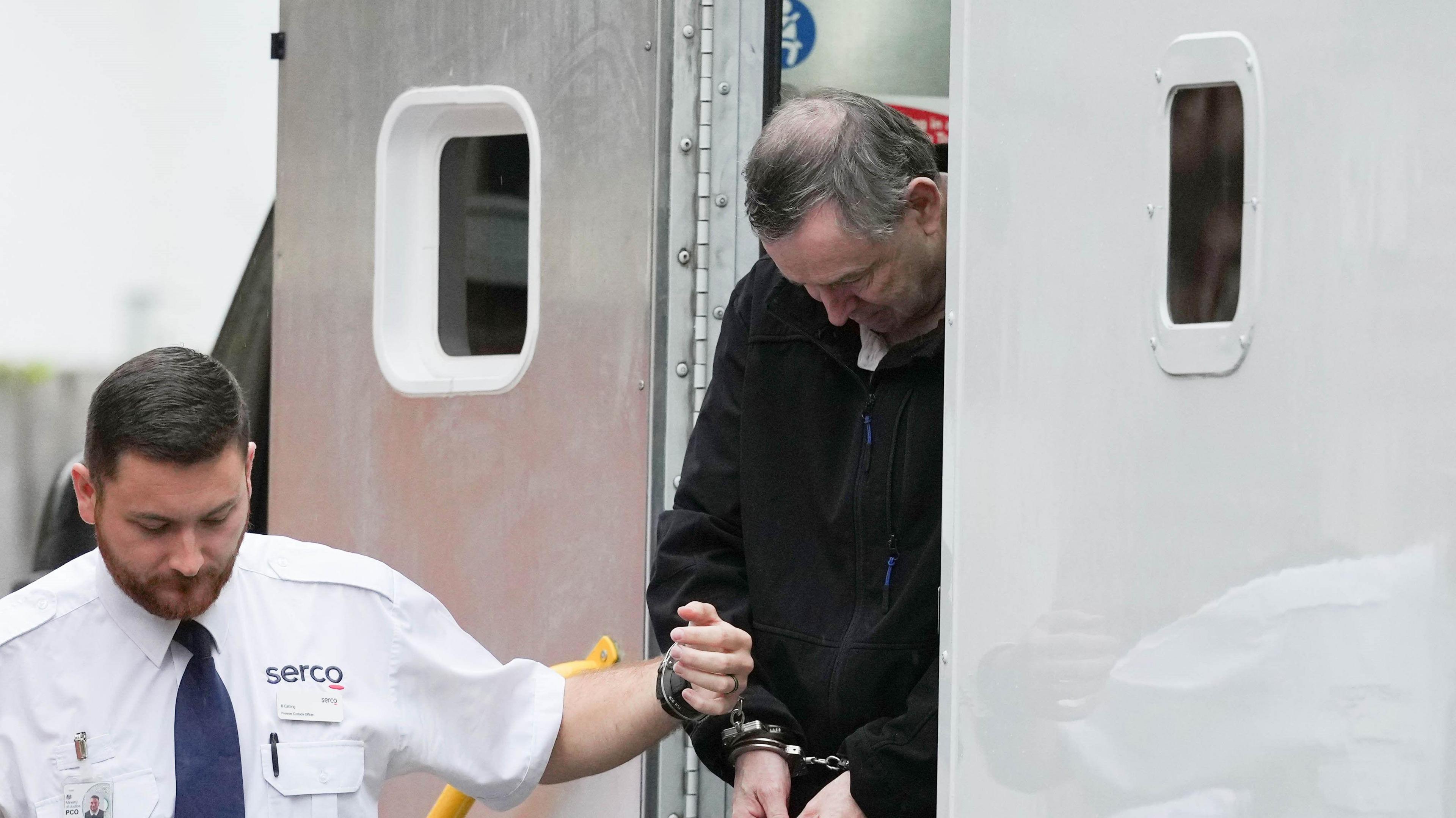 A balding man being taken out of a white prison van.