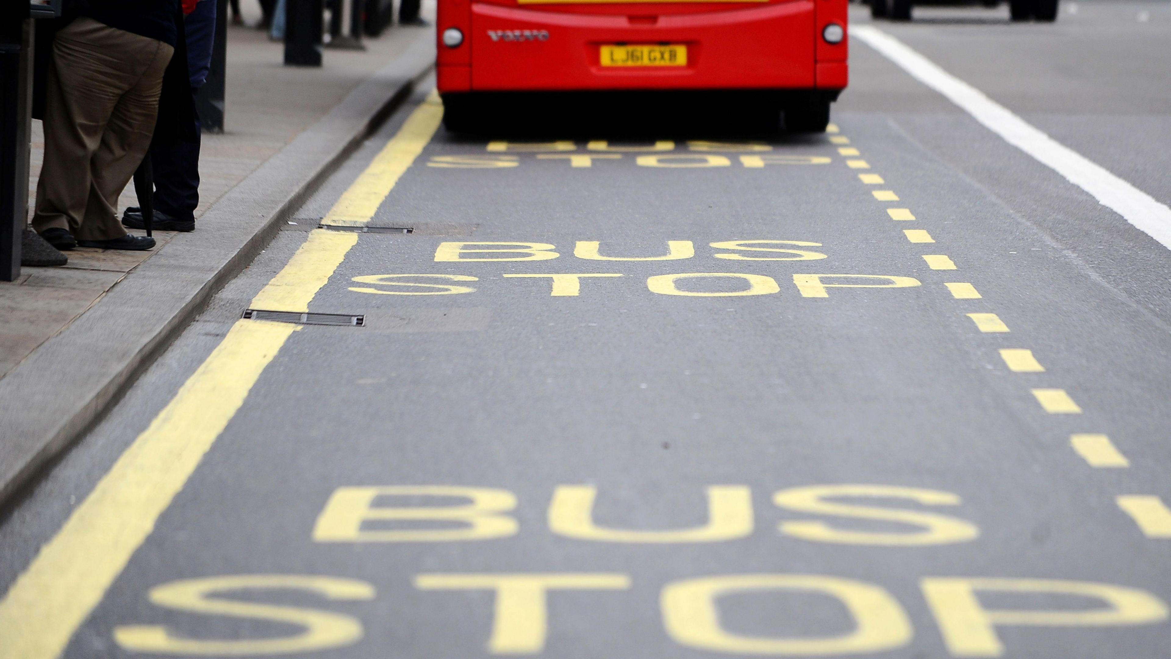 A close up of BUS STOP painted on a London road with yellow lines, the back of a bus is visible in the top of the image.