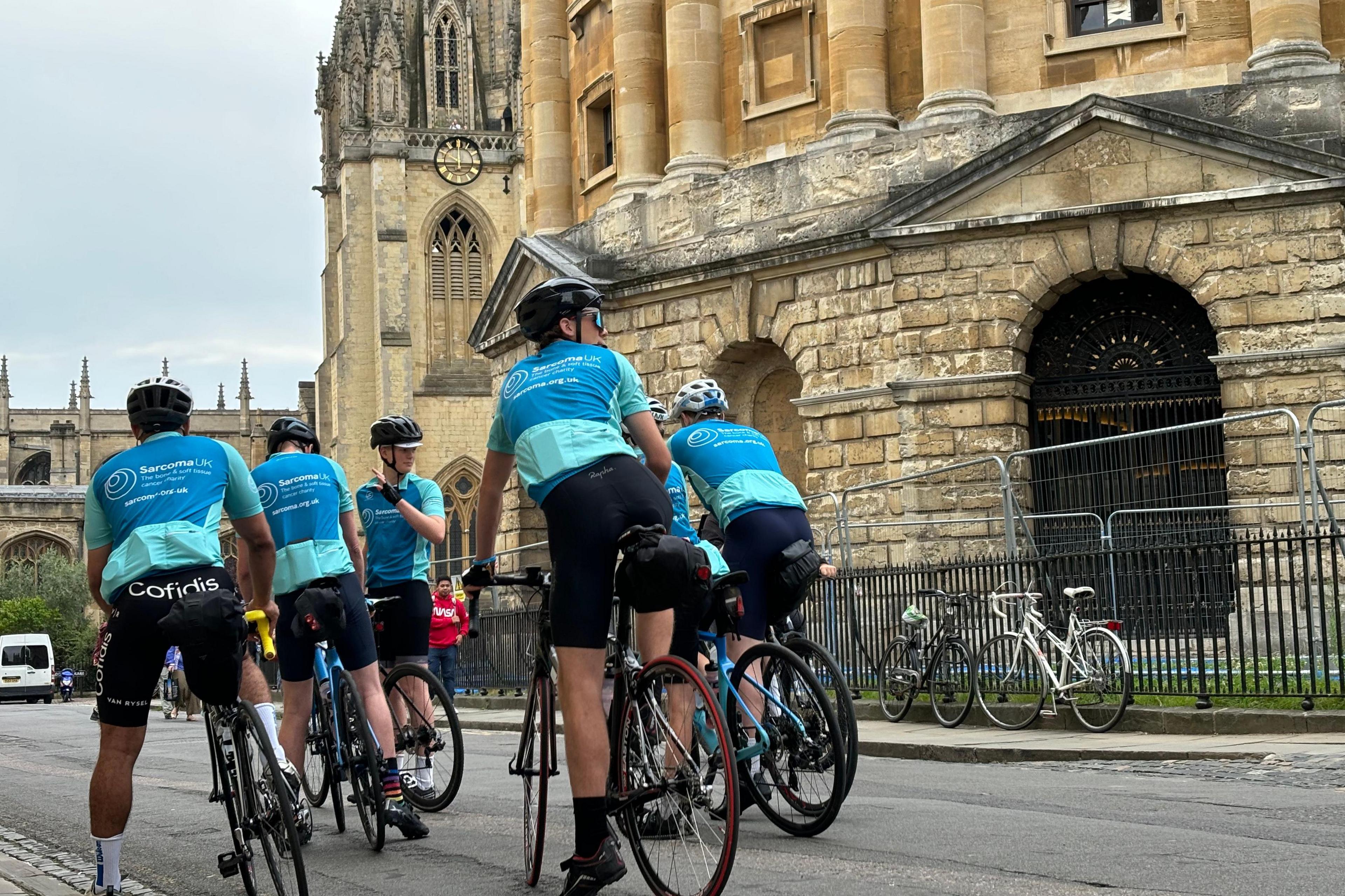 The cyclists are on the road next to the Radcliffe Camera, ready to set off.