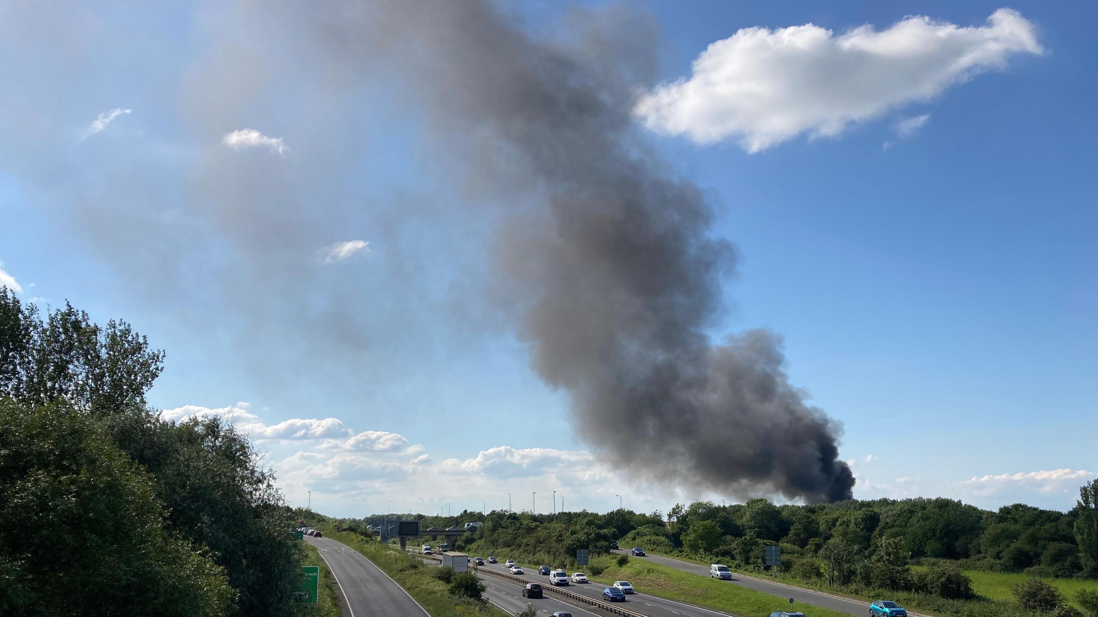 Large plume of black smoke rising above trees on the edge of the A14 near Milton, Cambridgeshire