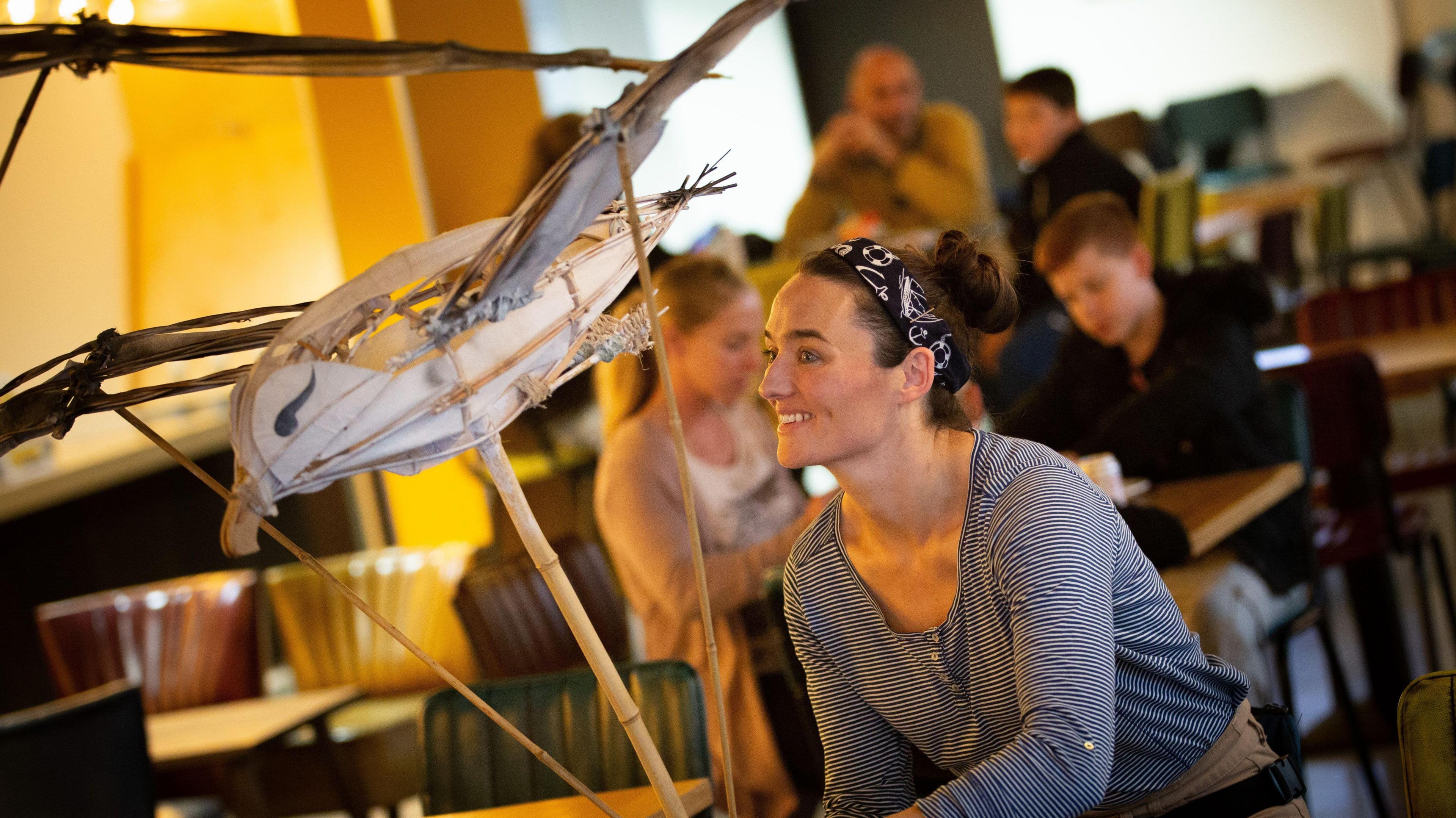 Anna holding a seagull puppet during a performance with her hair tied up in a bun smiling and looking off camera.